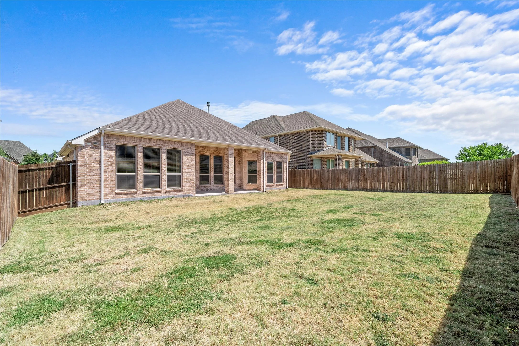 Expansive backyard with a full privacy fence, a brick exterior, multiple large windows, and a paved patio area