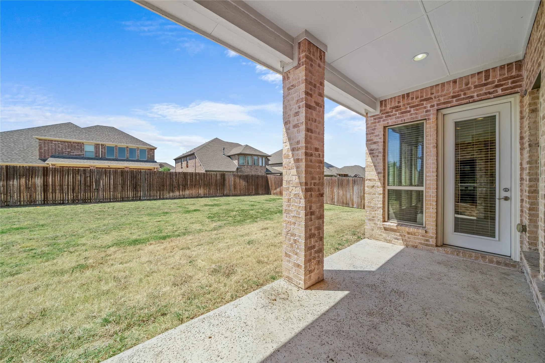 Covered patio featuring brick columns, recessed lighting, and a glass-paneled door