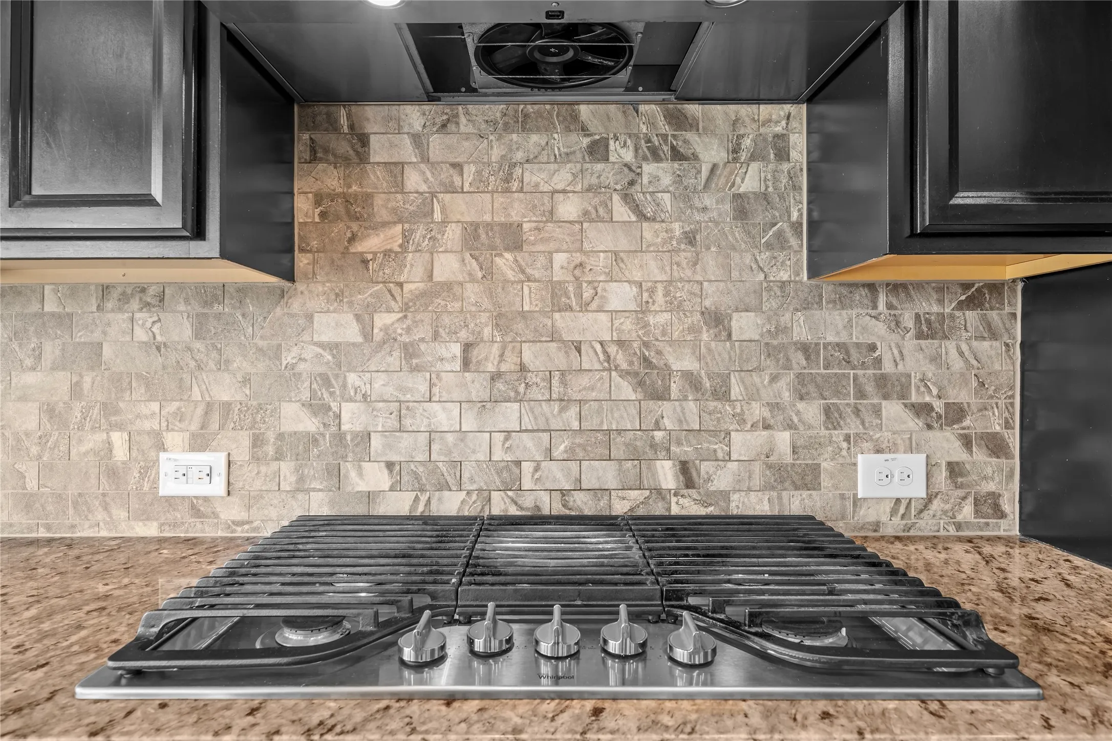 Stainless steel gas range, stone-finish backsplash, dark wood-finish cabinetry, and solid surface countertop