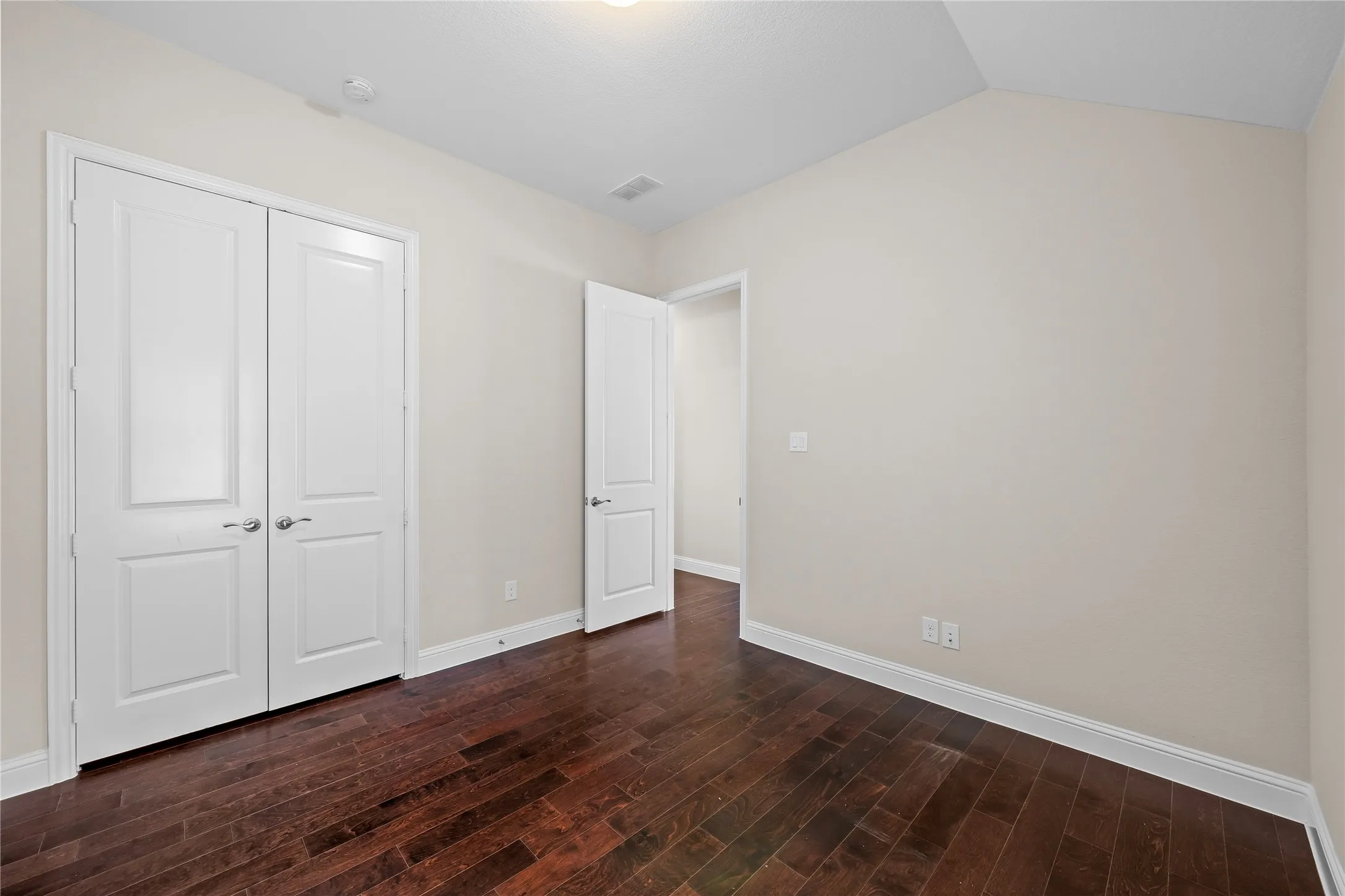 Dark wood-finish flooring with white trim, double panel doors, and a vaulted ceiling