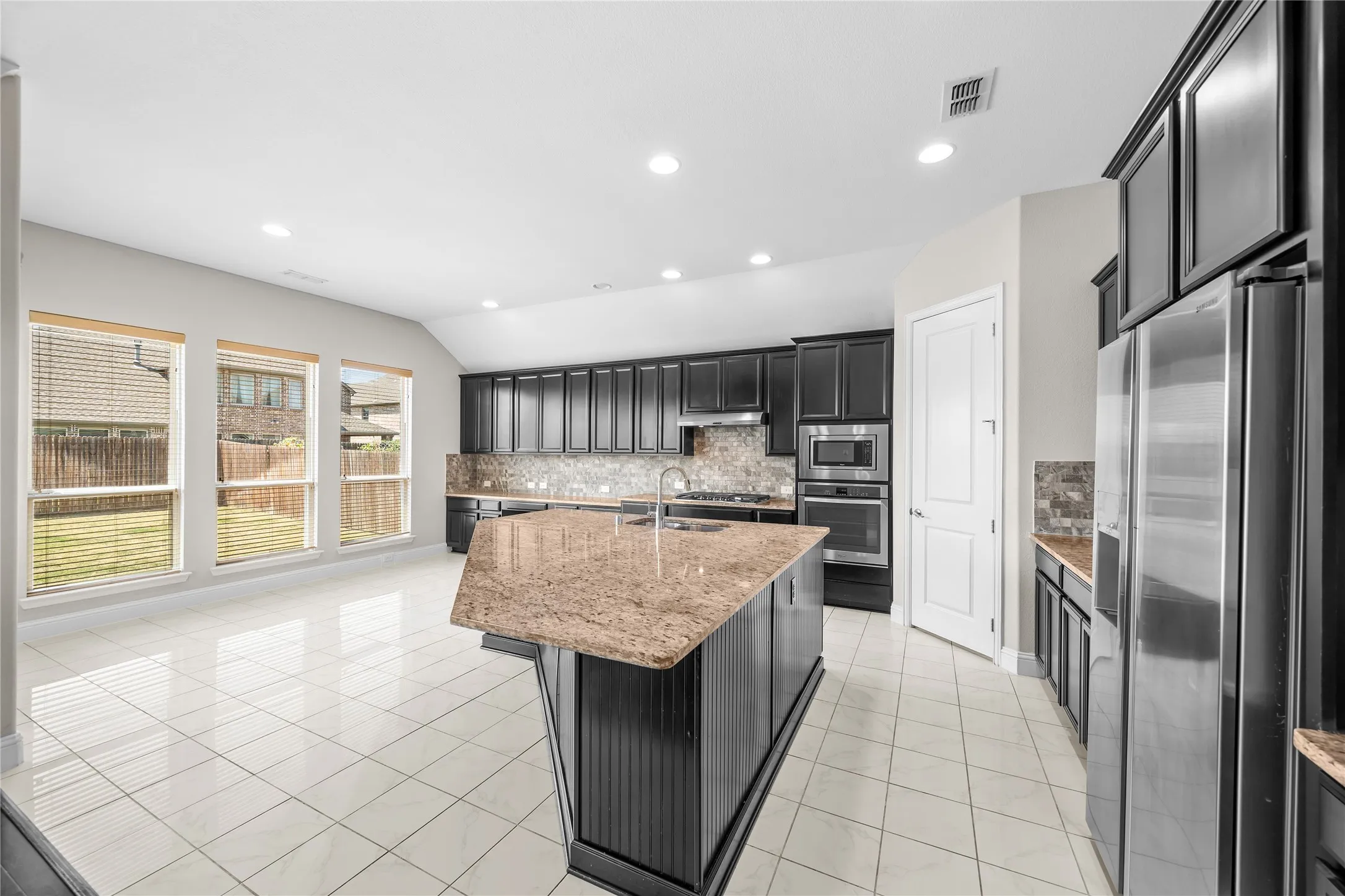 Spacious kitchen featuring an island with stone countertop, dark wood-finish cabinetry, stainless steel appliances, and tile flooring