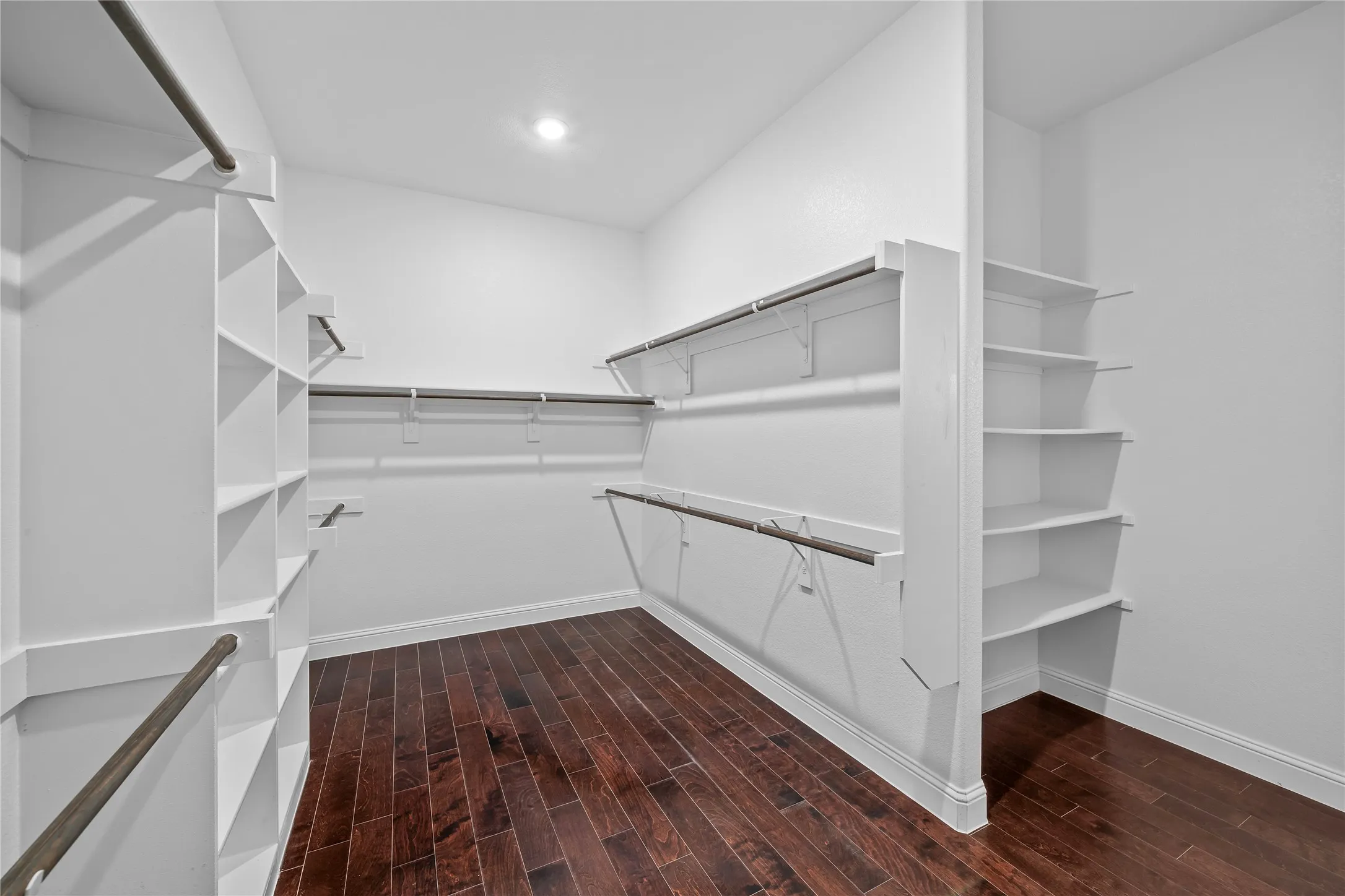Spacious walk-in closet featuring wood-finish flooring, extensive built-in shelving, multiple hanging rods, and recessed lighting