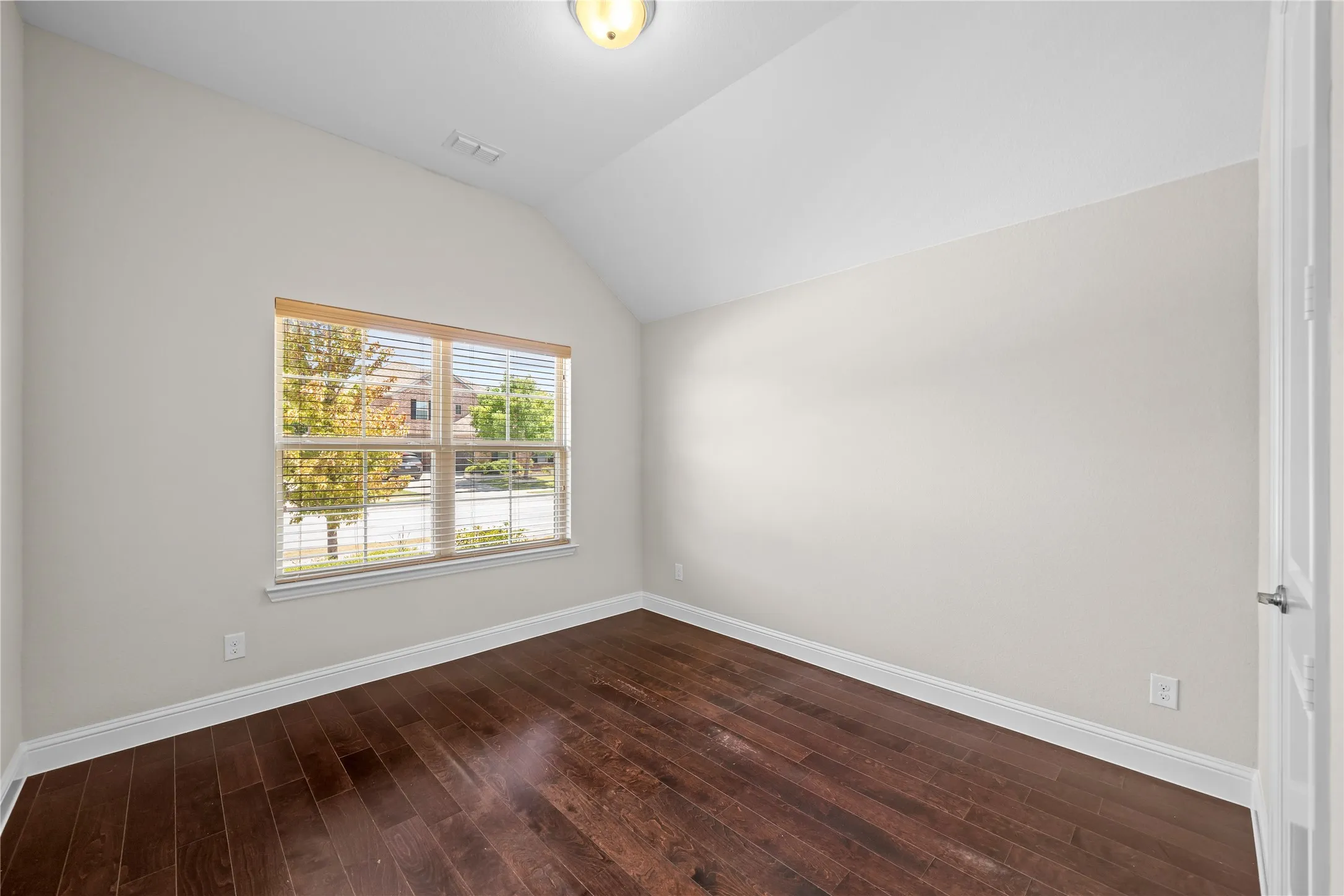 Vaulted ceiling, wood-finish flooring, single window with blinds, overhead light fixture, and white trim