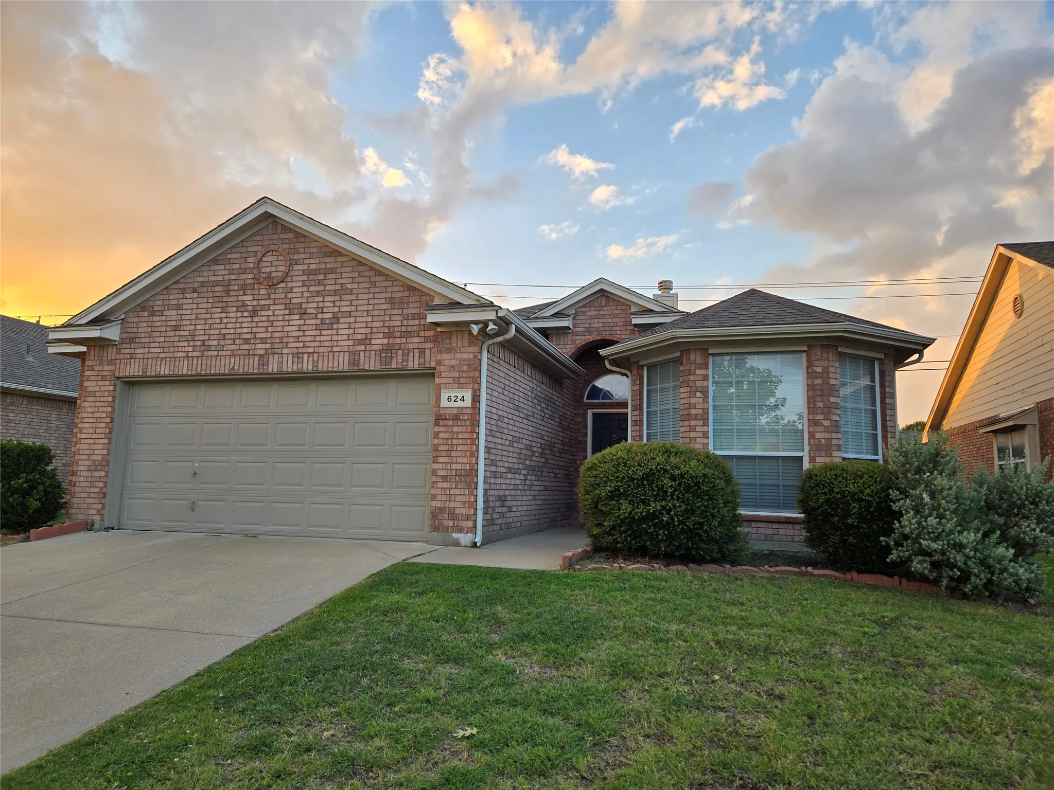 Ranch-style home featuring an attached garage, a front lawn, concrete driveway, and brick siding