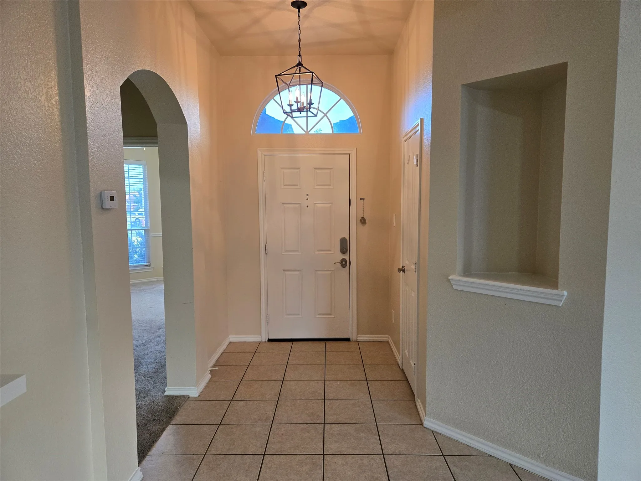 Entrance foyer with arched walkways, a textured wall, and light tile patterned floors