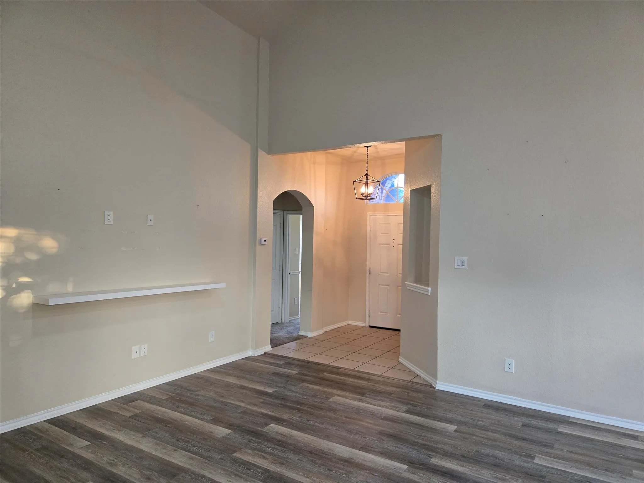 Spare room with arched walkways, wood finished floors, a towering ceiling, and a chandelier