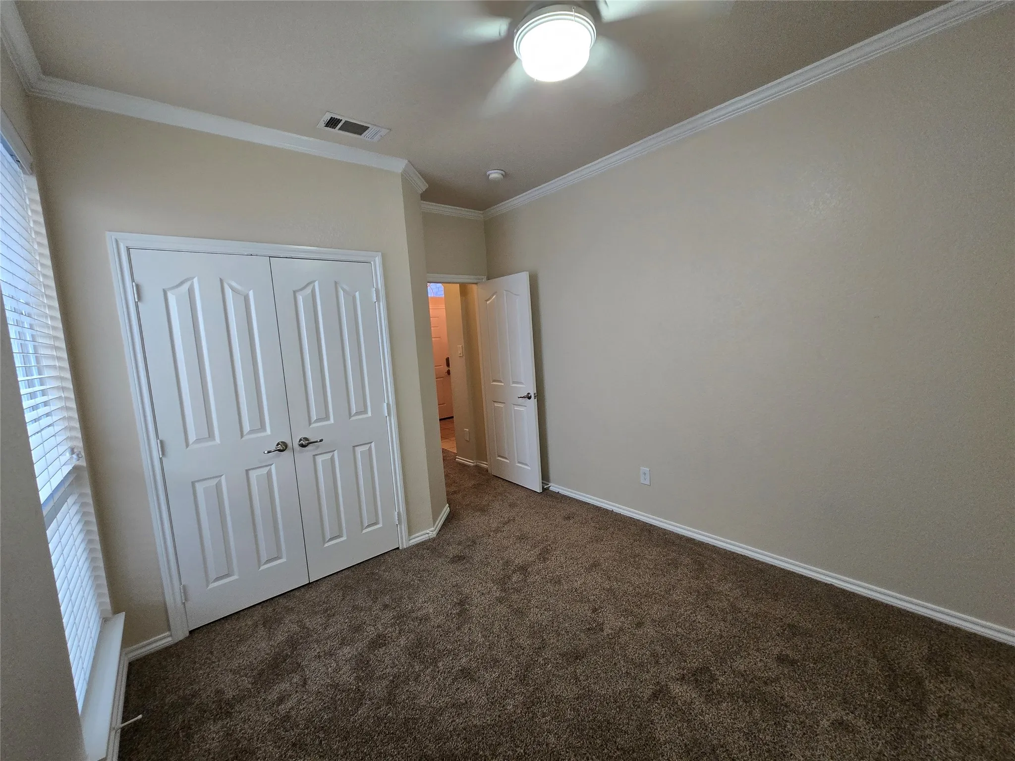 Unfurnished bedroom with crown molding, dark colored carpet, a closet, and a ceiling fan