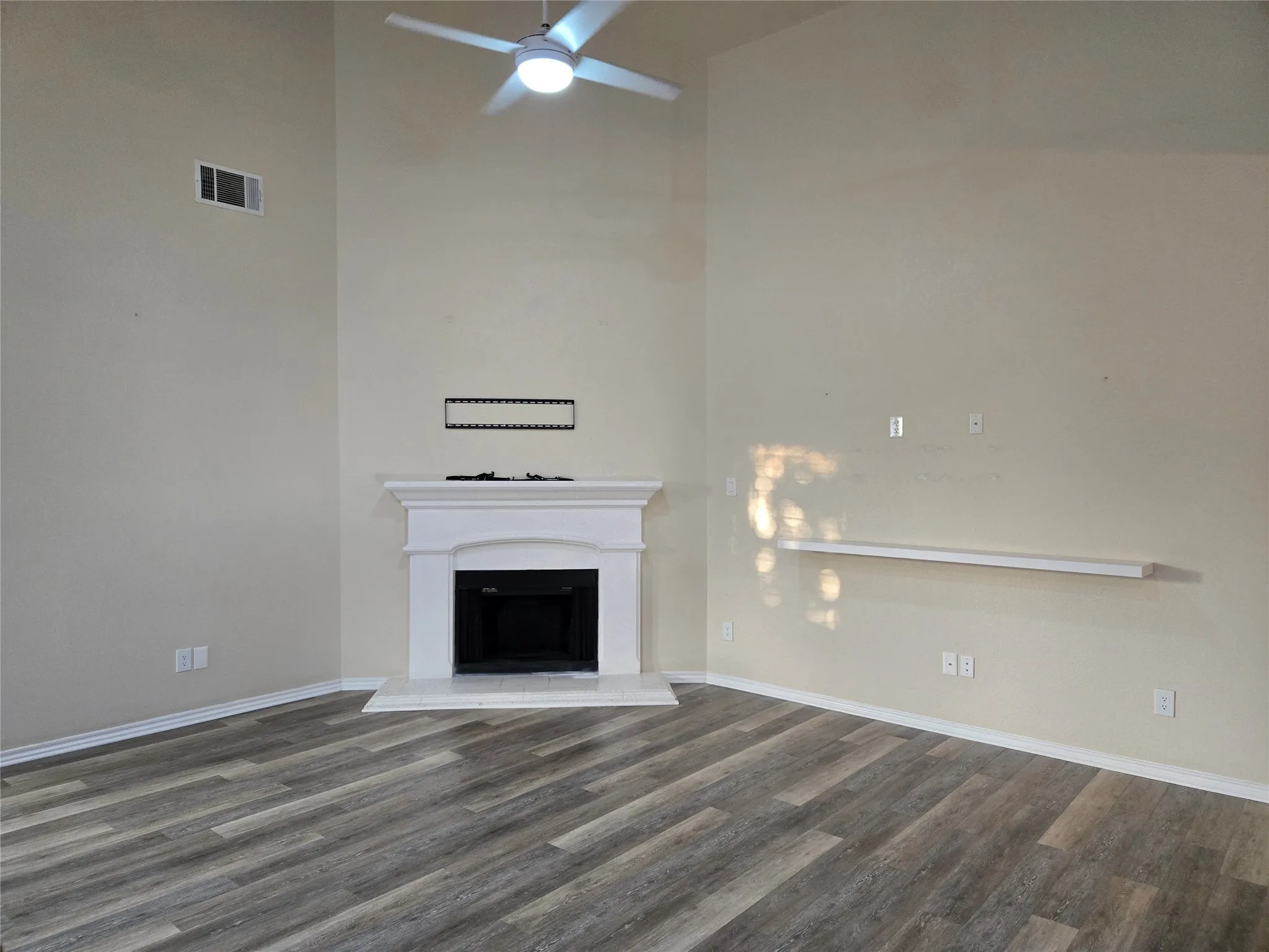 Unfurnished living room with a fireplace with raised hearth, a towering ceiling, dark wood finished floors, and a ceiling fan