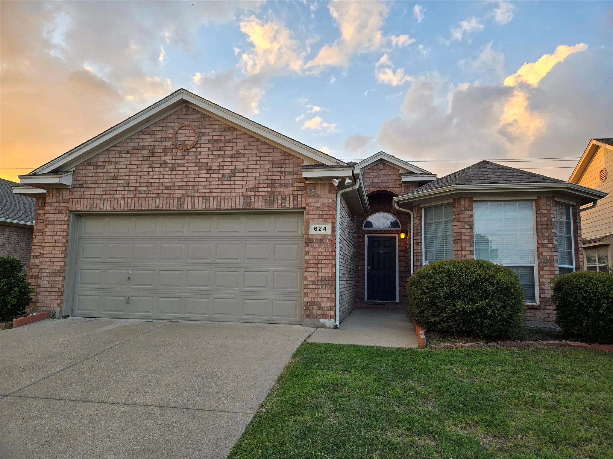Ranch-style home featuring a garage, brick siding, driveway, and a front yard