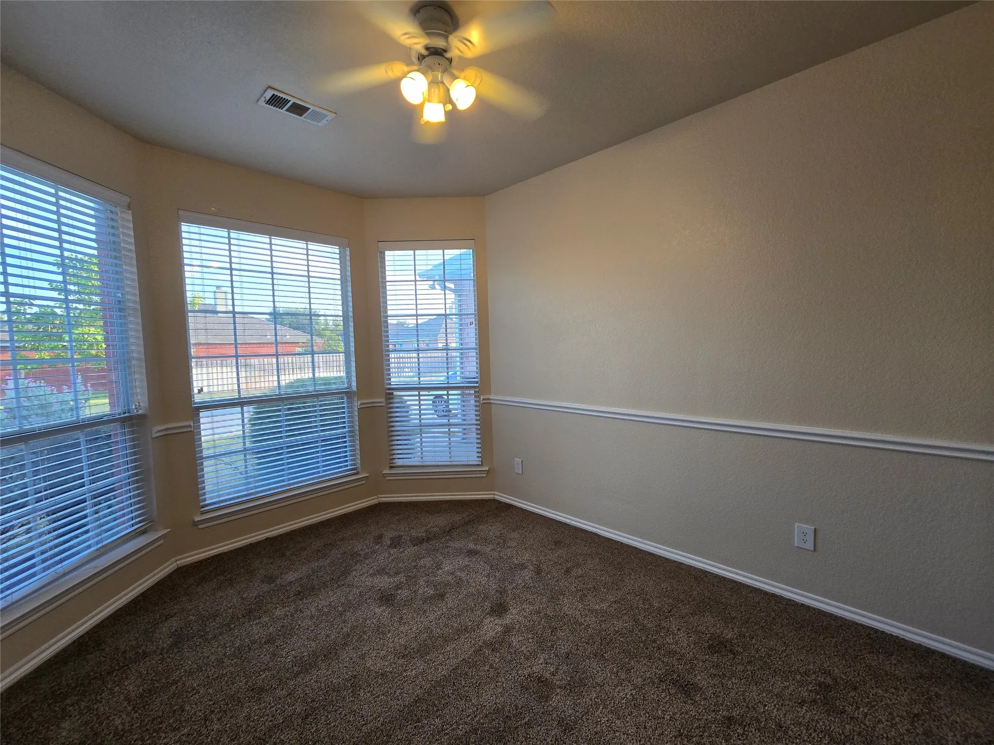 Empty room featuring dark colored carpet and a ceiling fan