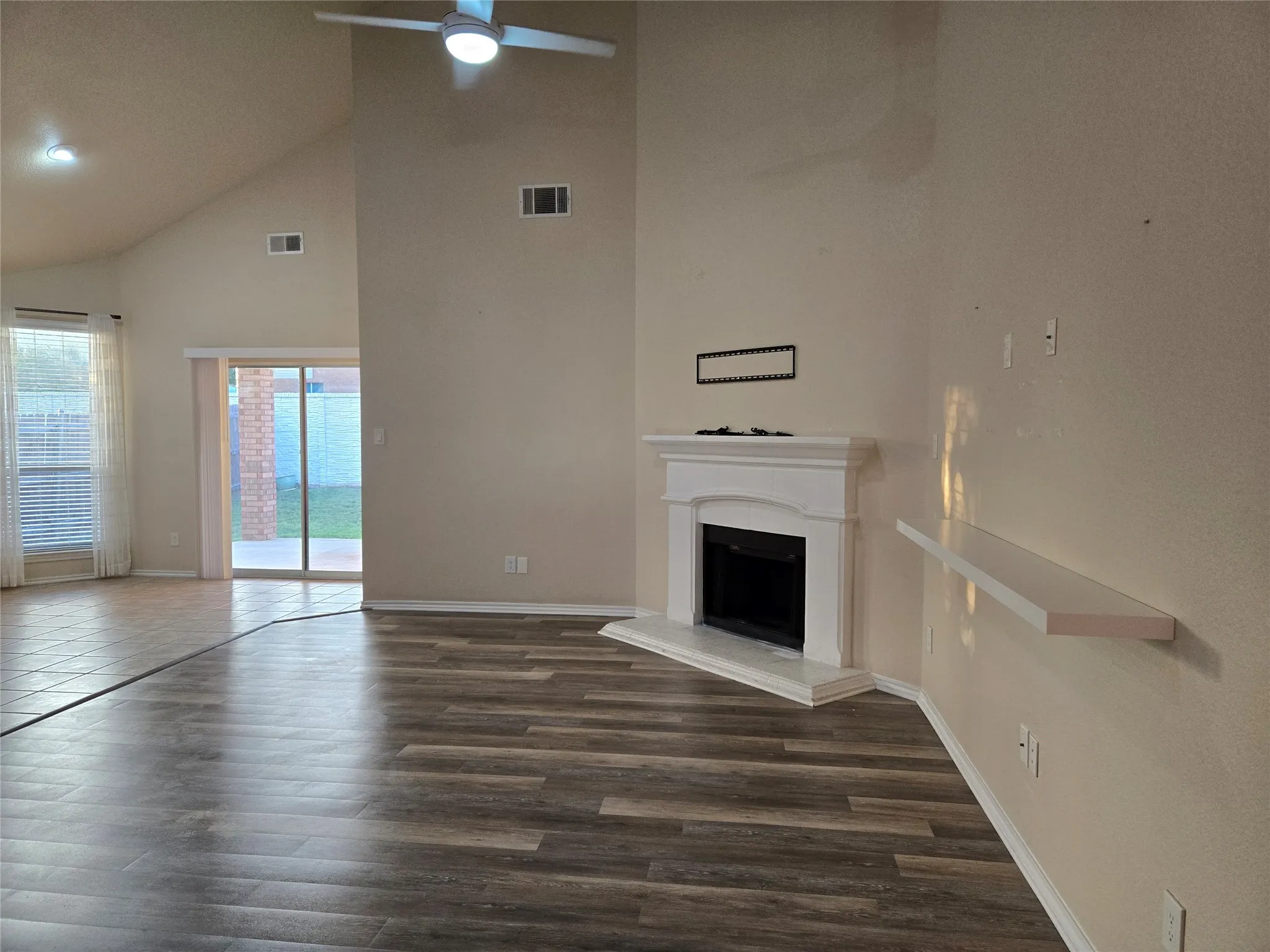 Unfurnished living room with high vaulted ceiling, dark wood-style floors, a fireplace with raised hearth, and ceiling fan