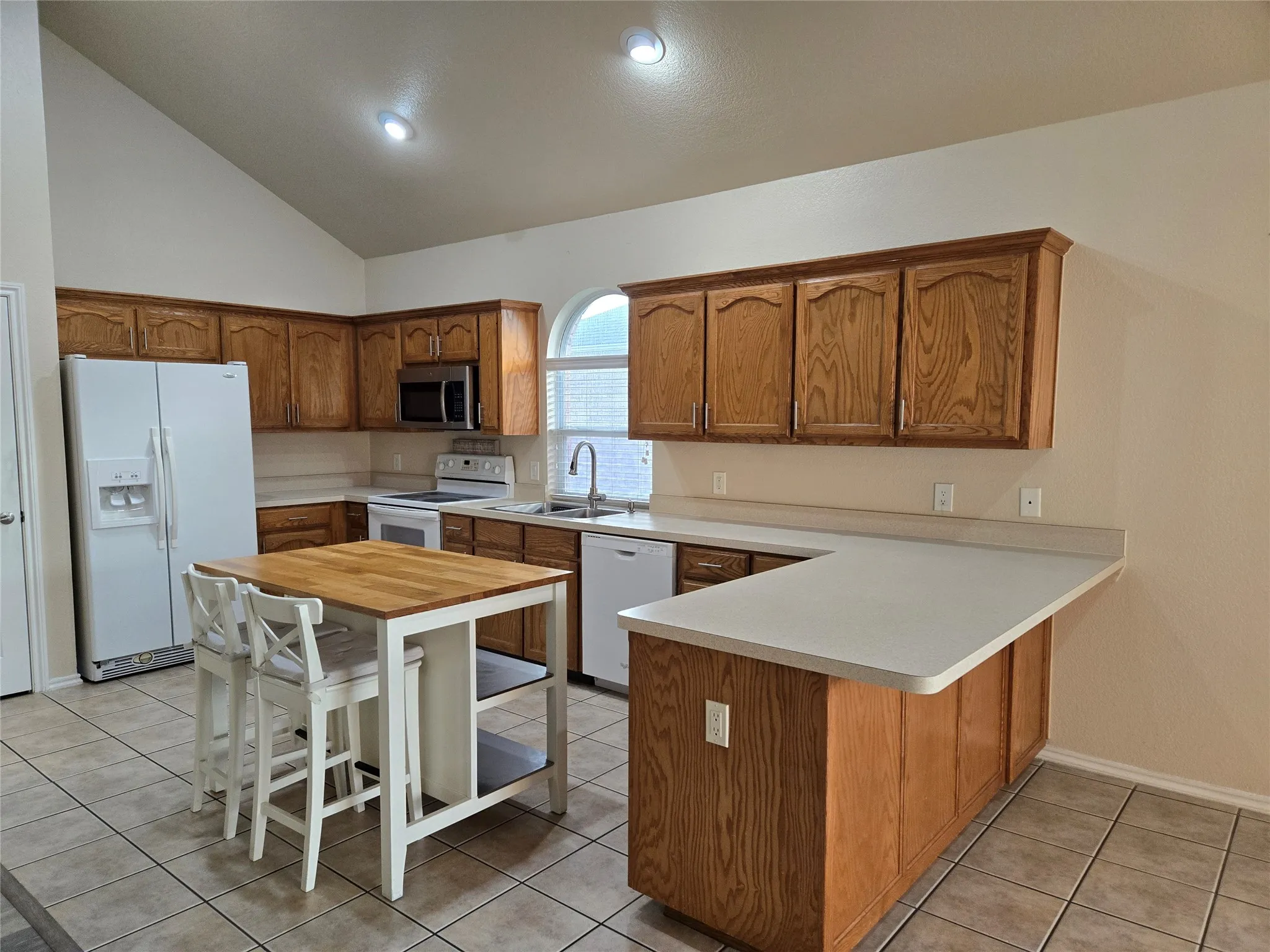 Kitchen with light countertops, brown cabinetry, white appliances, light tile patterned floors, and a peninsula