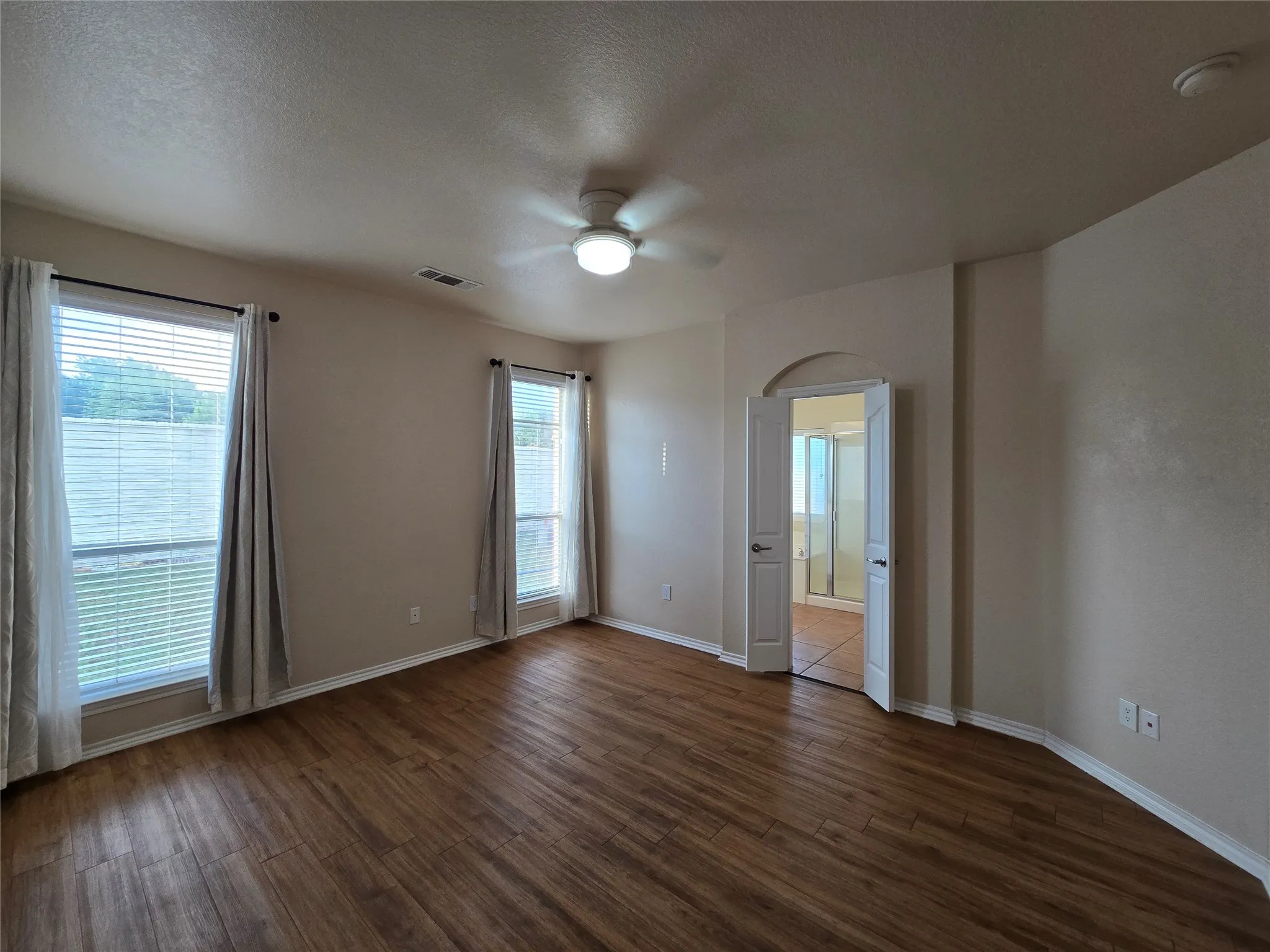 Empty room featuring healthy amount of natural light, a ceiling fan, a textured ceiling, and dark wood-style flooring