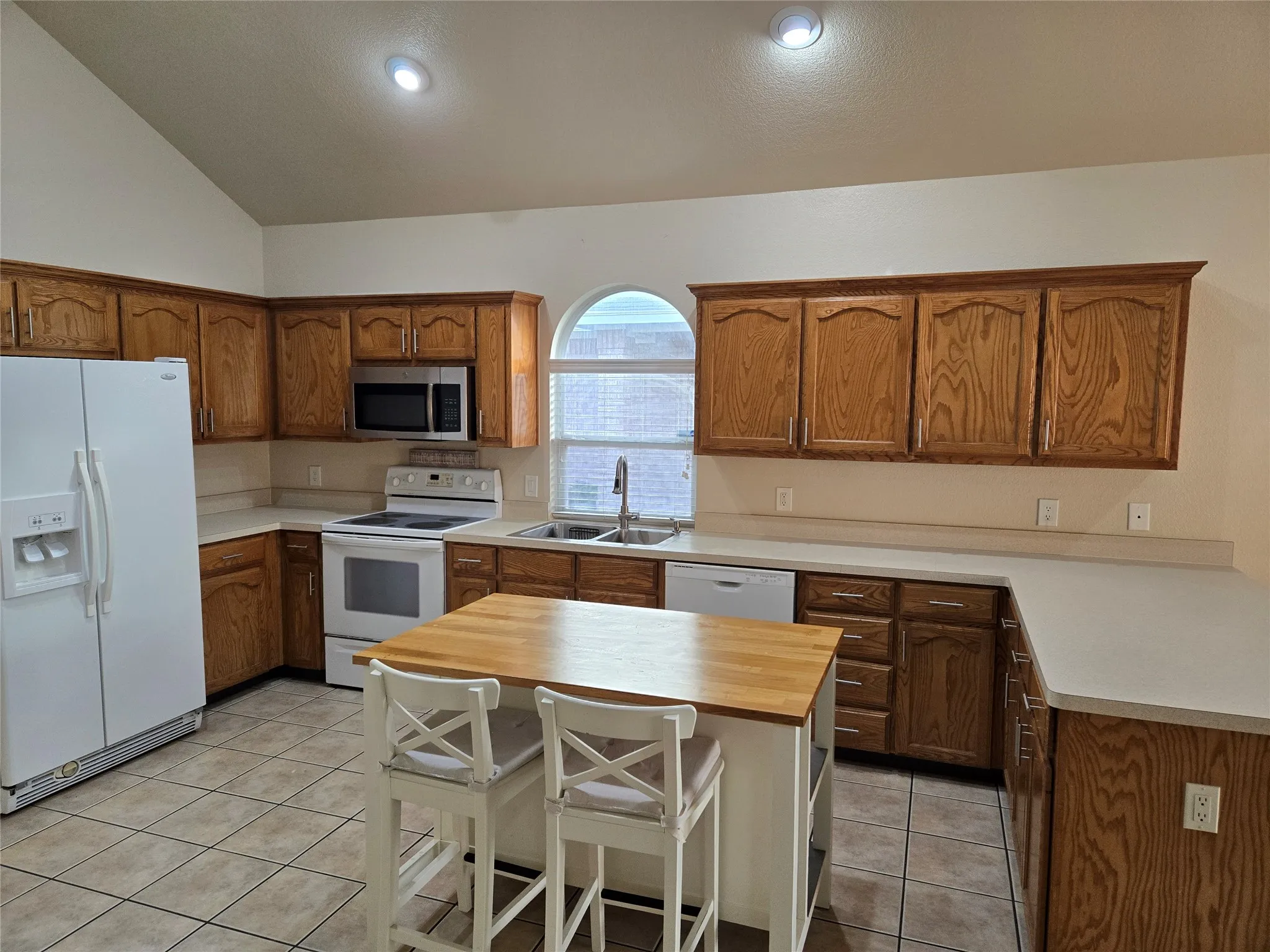 Kitchen with white appliances, light tile patterned floors, brown cabinets, a kitchen breakfast bar, and recessed lighting