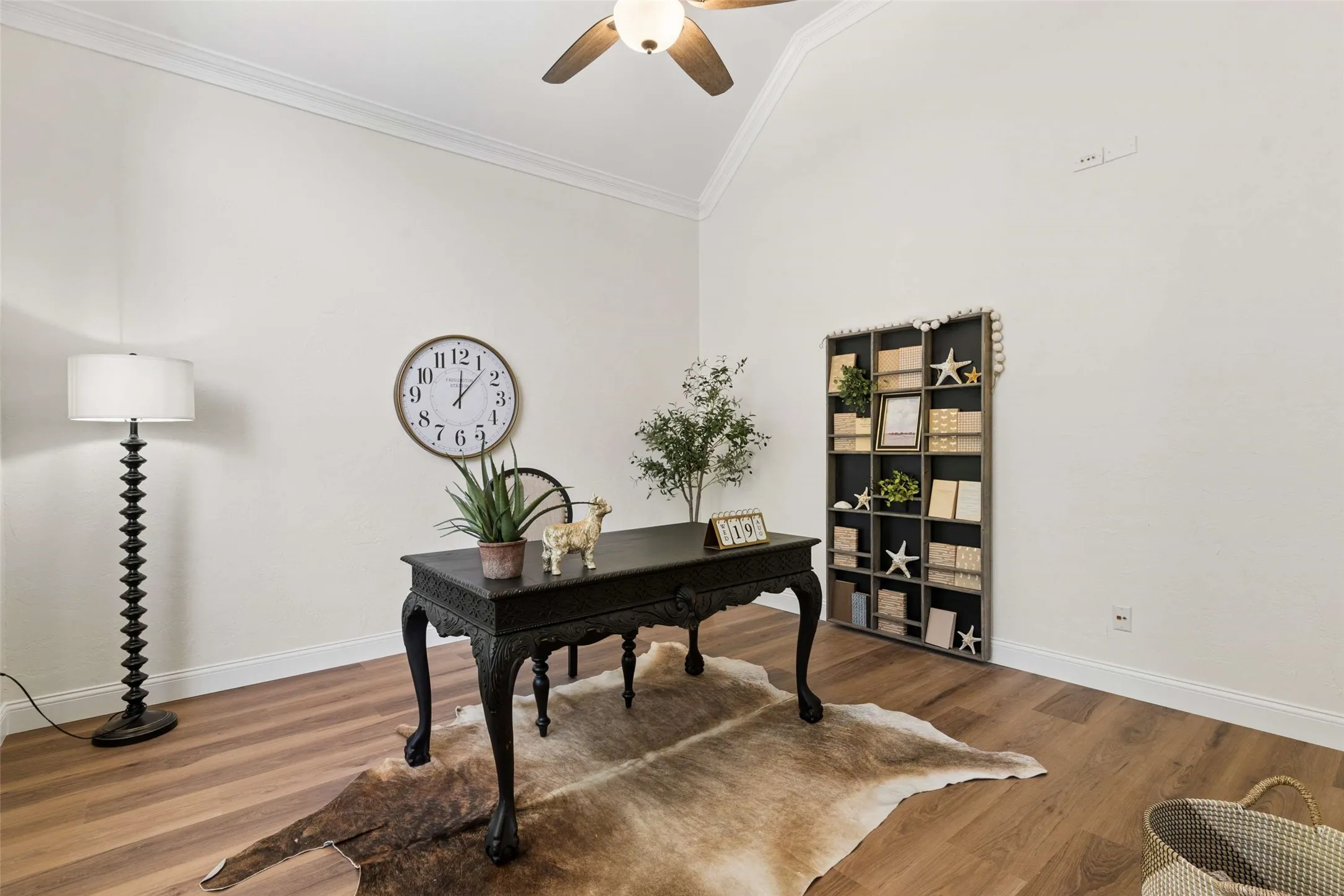 Vaulted ceiling with crown molding, wood-finish flooring, ceiling fan with integrated lighting, built-in shelving, and light-toned walls