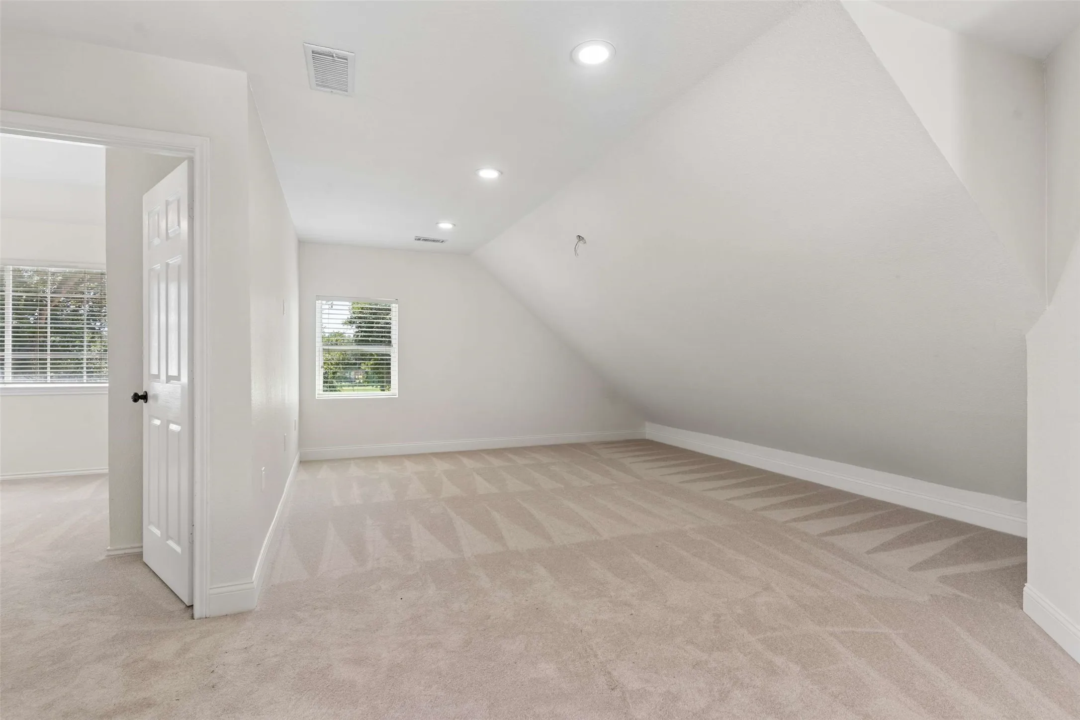 Spacious carpeted room with a sloped ceiling and recessed lighting