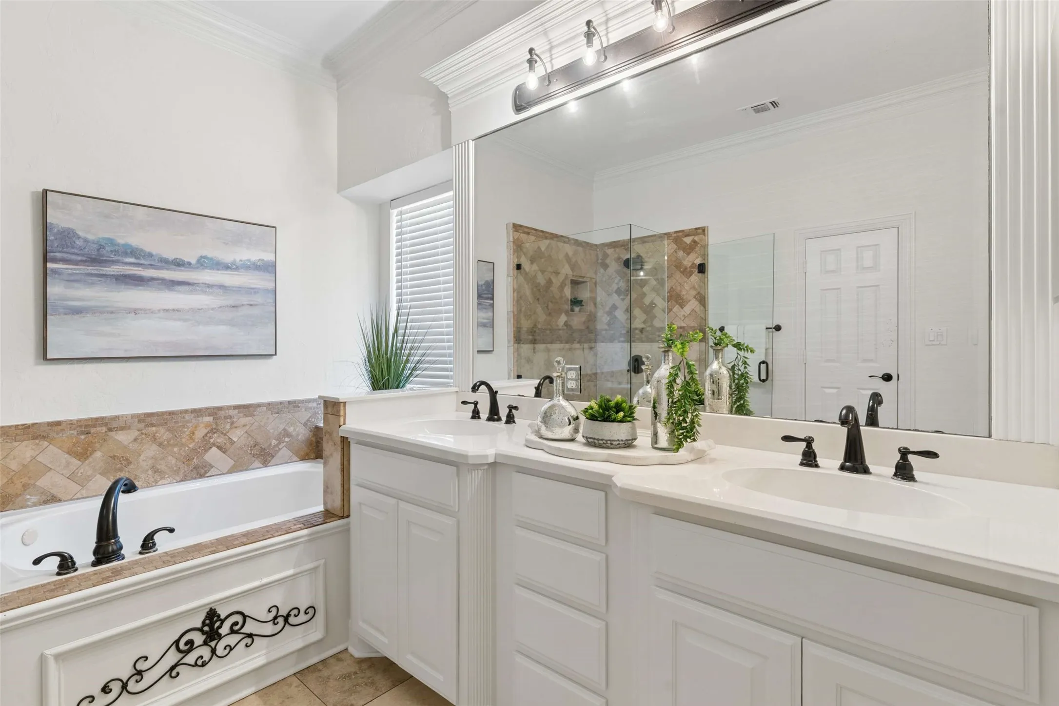 Dual vanity with white cabinetry, built-in soaking tub with stone tile surround, individual undermount sinks, and a framed mirror with integrated lighting