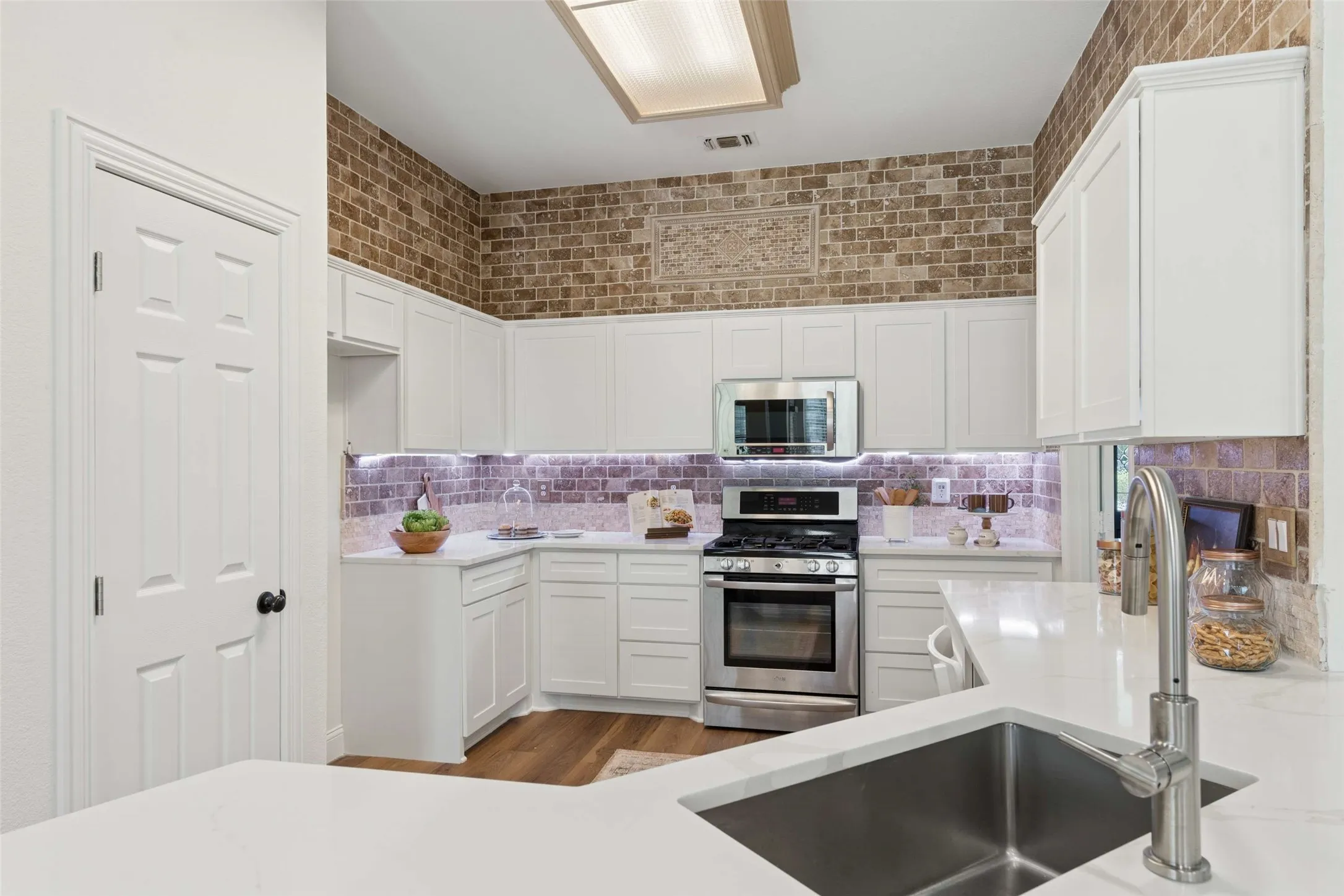 Kitchen featuring white cabinetry, stainless steel appliances, a multi-tone tile backsplash, and solid surface countertops