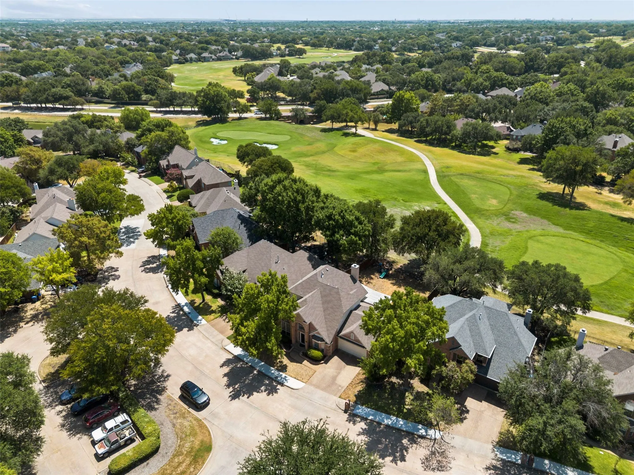 Residential street with mature tree canopy, curved paved roads, and manicured golf course greens