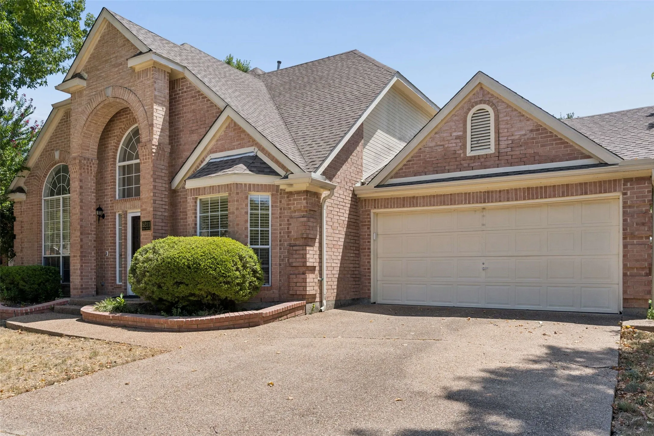 Brick facade residence featuring an arched entryway, multiple gables, bay windows, and an attached two-car garage