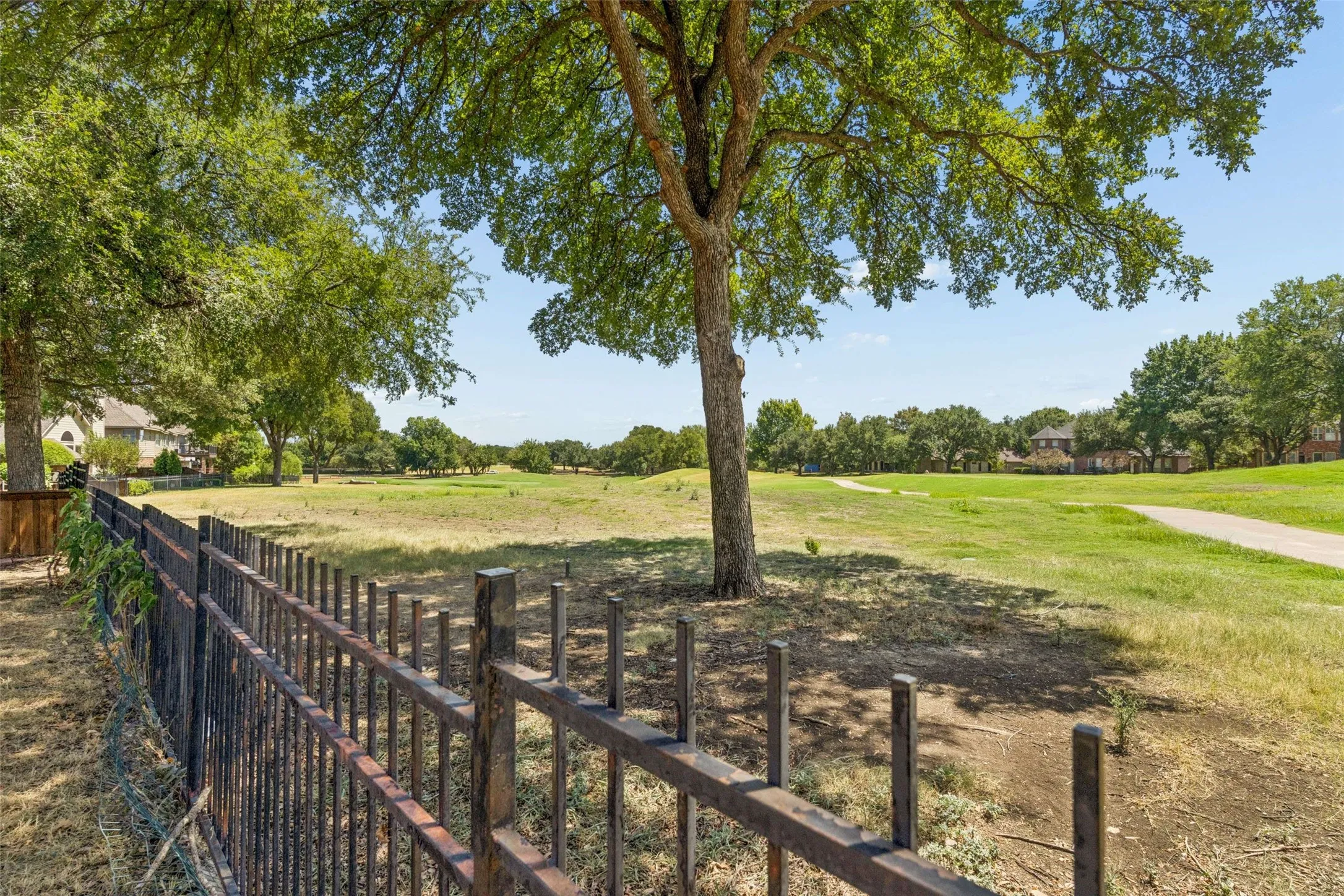 Expansive grounds featuring a mature tree, wrought iron fencing, and distant residential structures