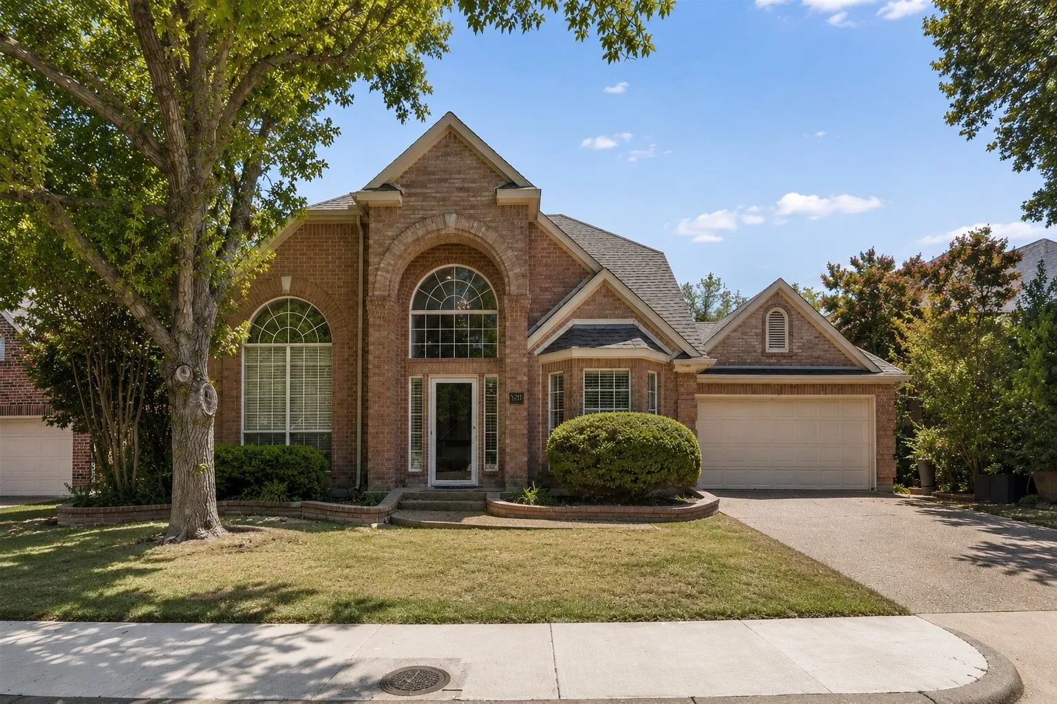 Brick exterior with arched windows, an attached two-car garage, and a concrete driveway