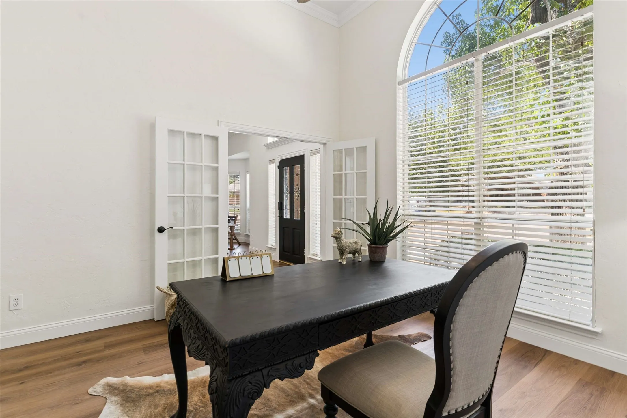 Arched picture window with blinds, wood-finish flooring, white French doors, and high ceilings