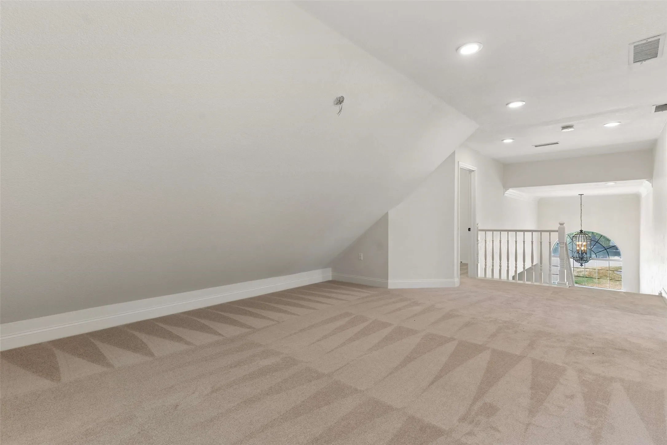Carpeted loft space featuring sloped ceilings, recessed lighting, white railing, and an arched window