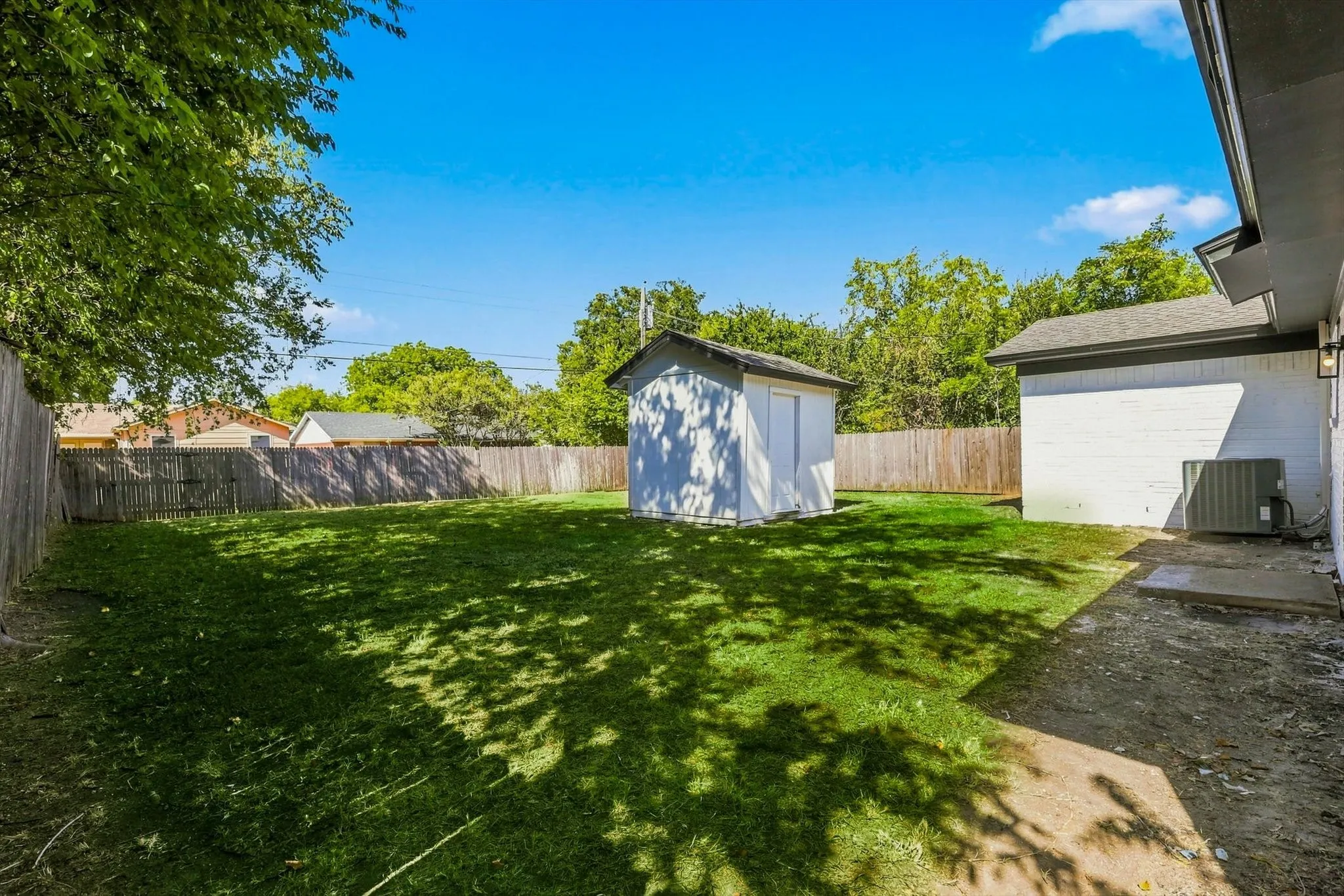 Expansive backyard featuring a lush lawn, privacy fencing, and a detached storage shed