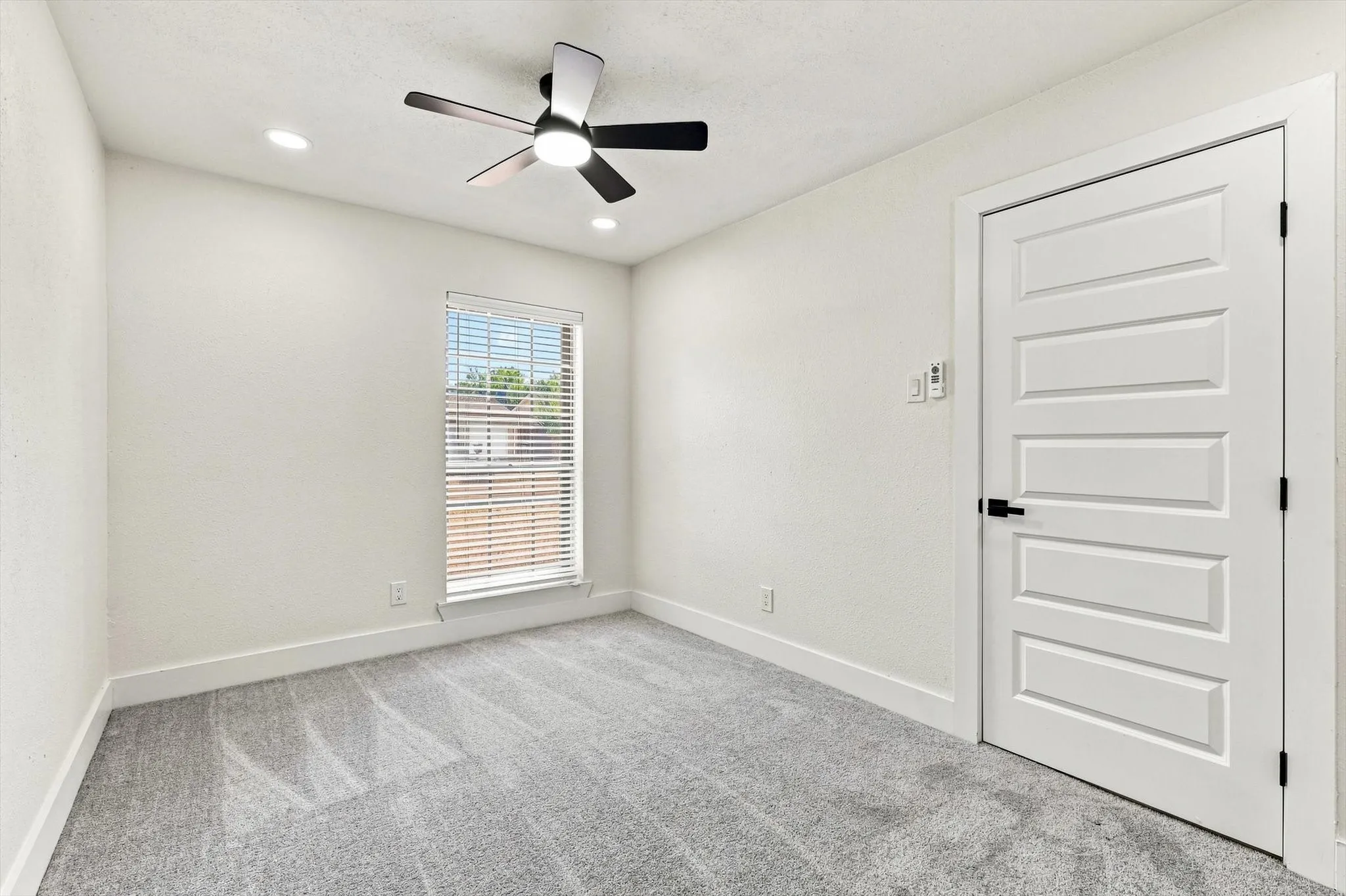 Recessed lighting, ceiling fan with integrated light, carpeted flooring, window with horizontal blinds, and a paneled interior door with matte black hardware