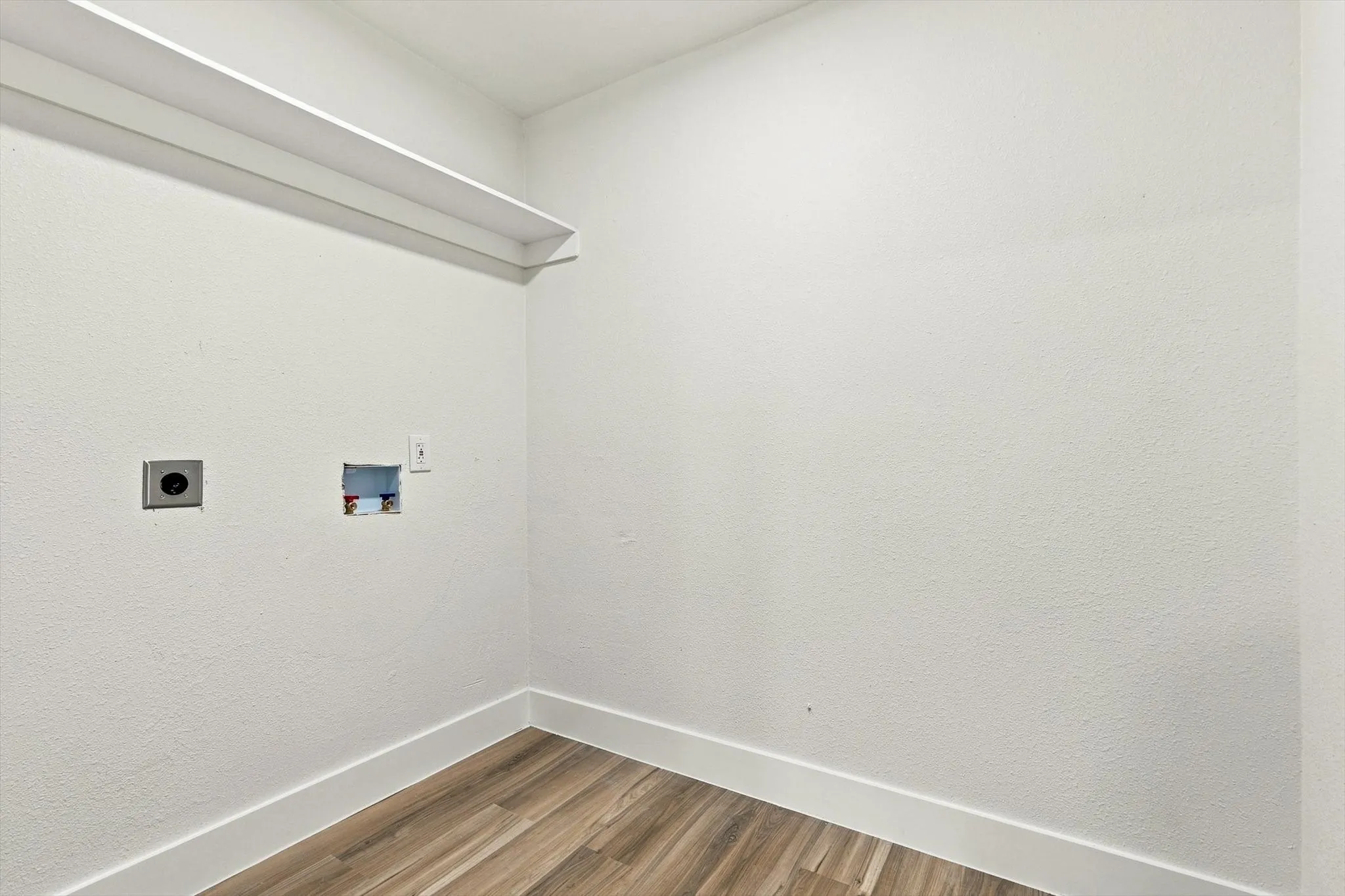 Wood-finish flooring with white baseboards, white walls, and a white overhead shelf
