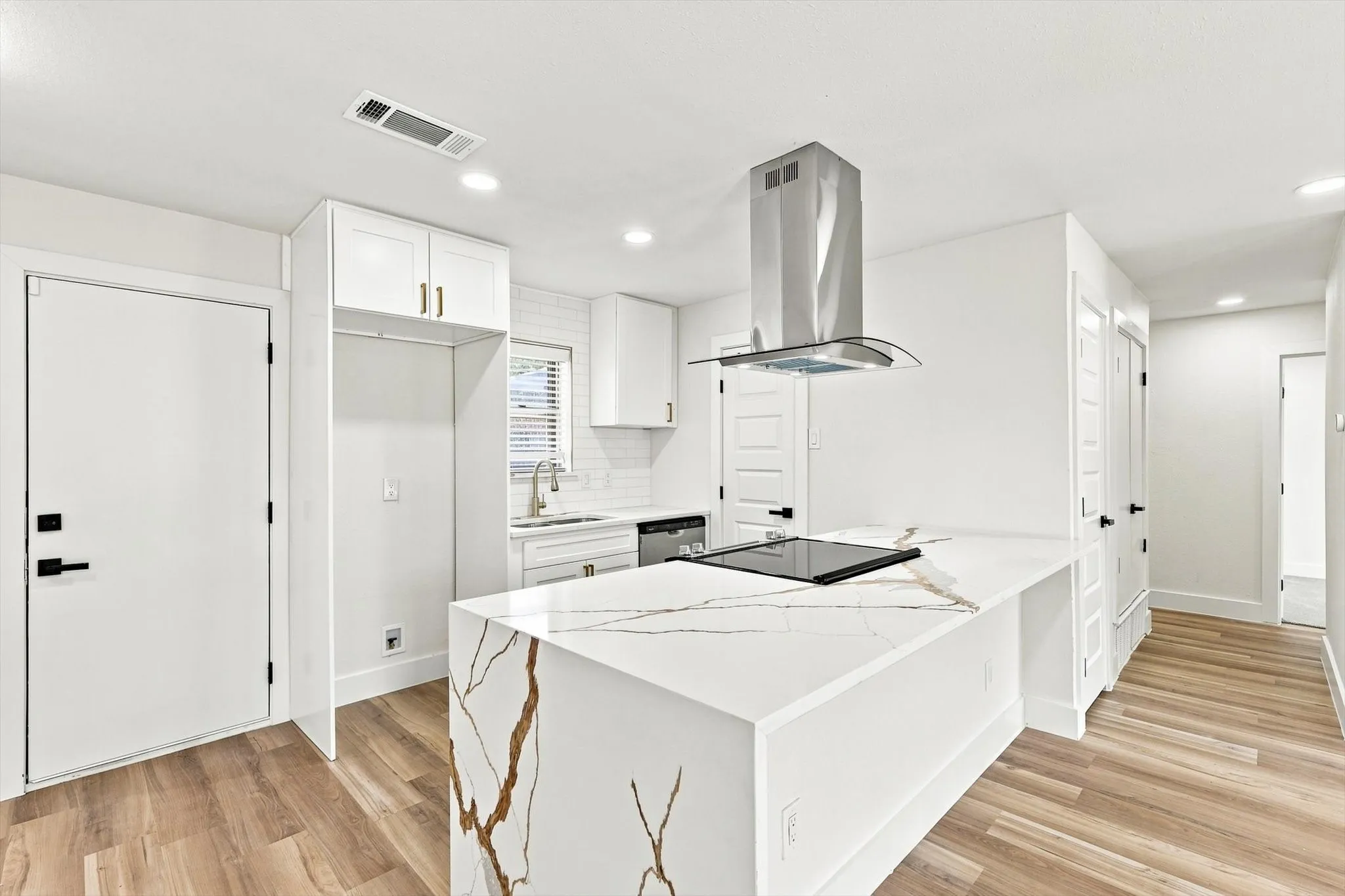 Kitchen featuring a waterfall island with stone countertop, built-in cooktop, stainless steel range hood, and white cabinetry