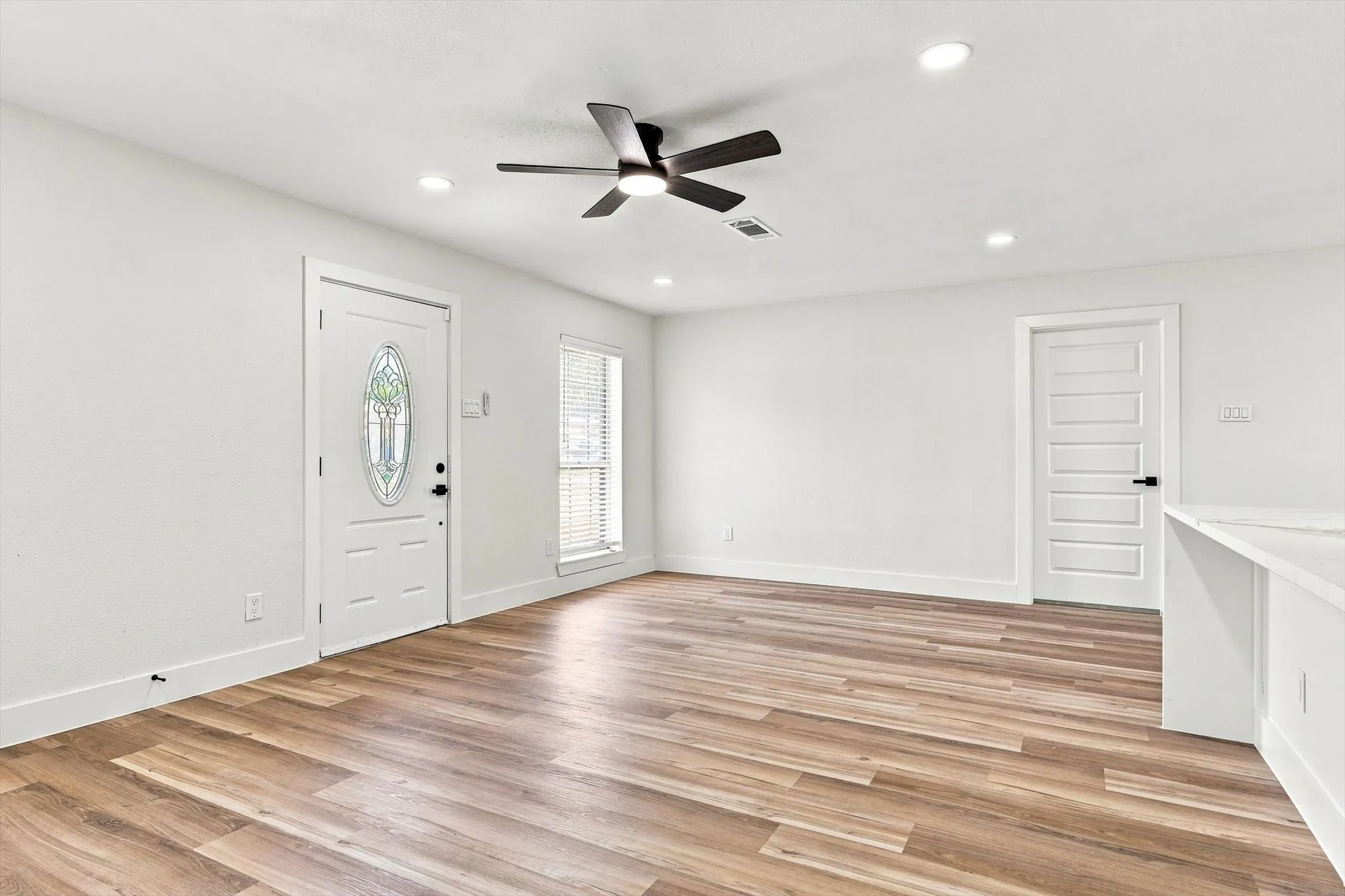 Light-filled interior featuring wood-finish flooring, white walls, recessed lighting, and a ceiling fan