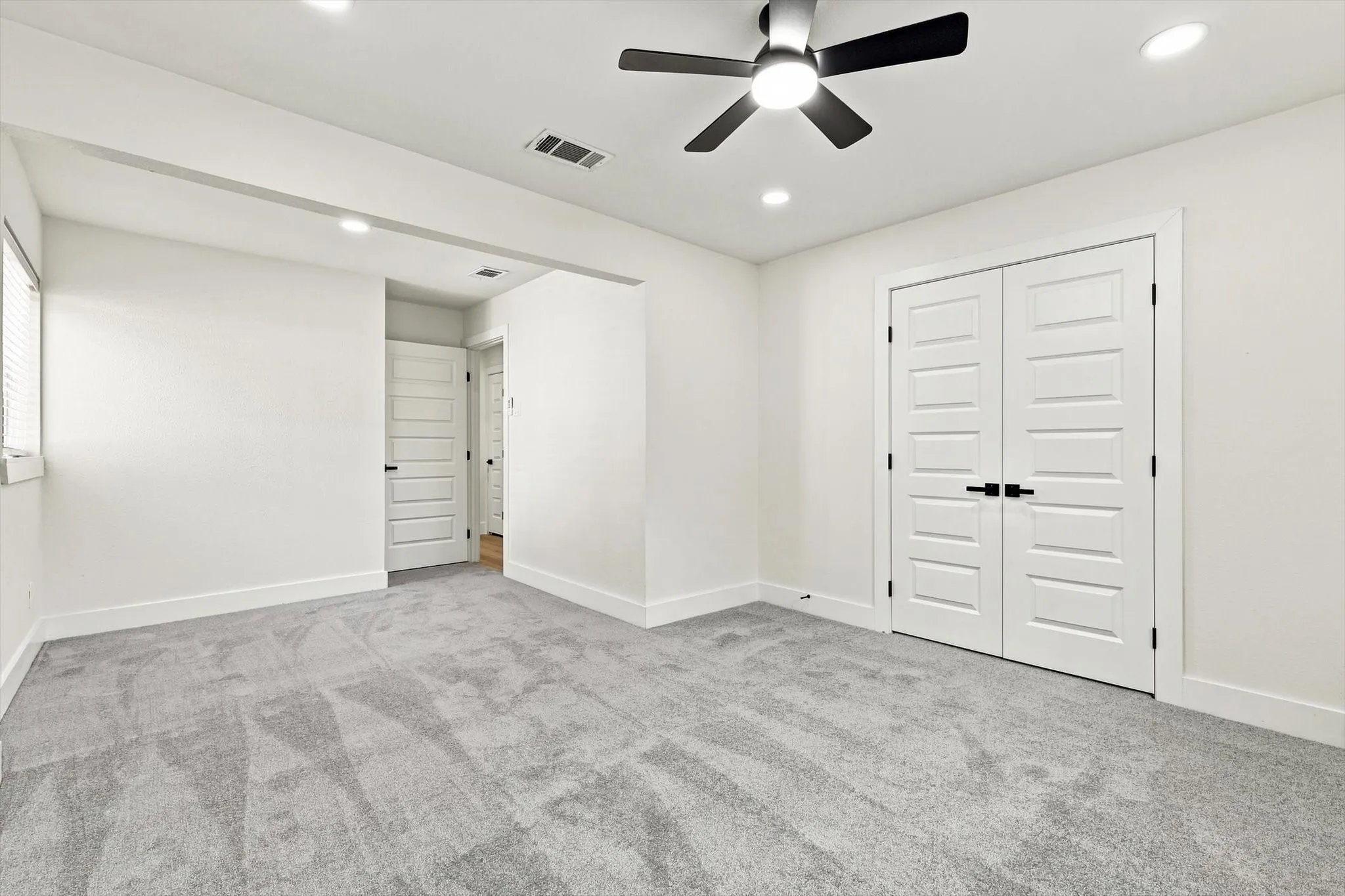 Plush gray carpeting, recessed ceiling lighting, a modern ceiling fan, and white paneled doors with black hardware