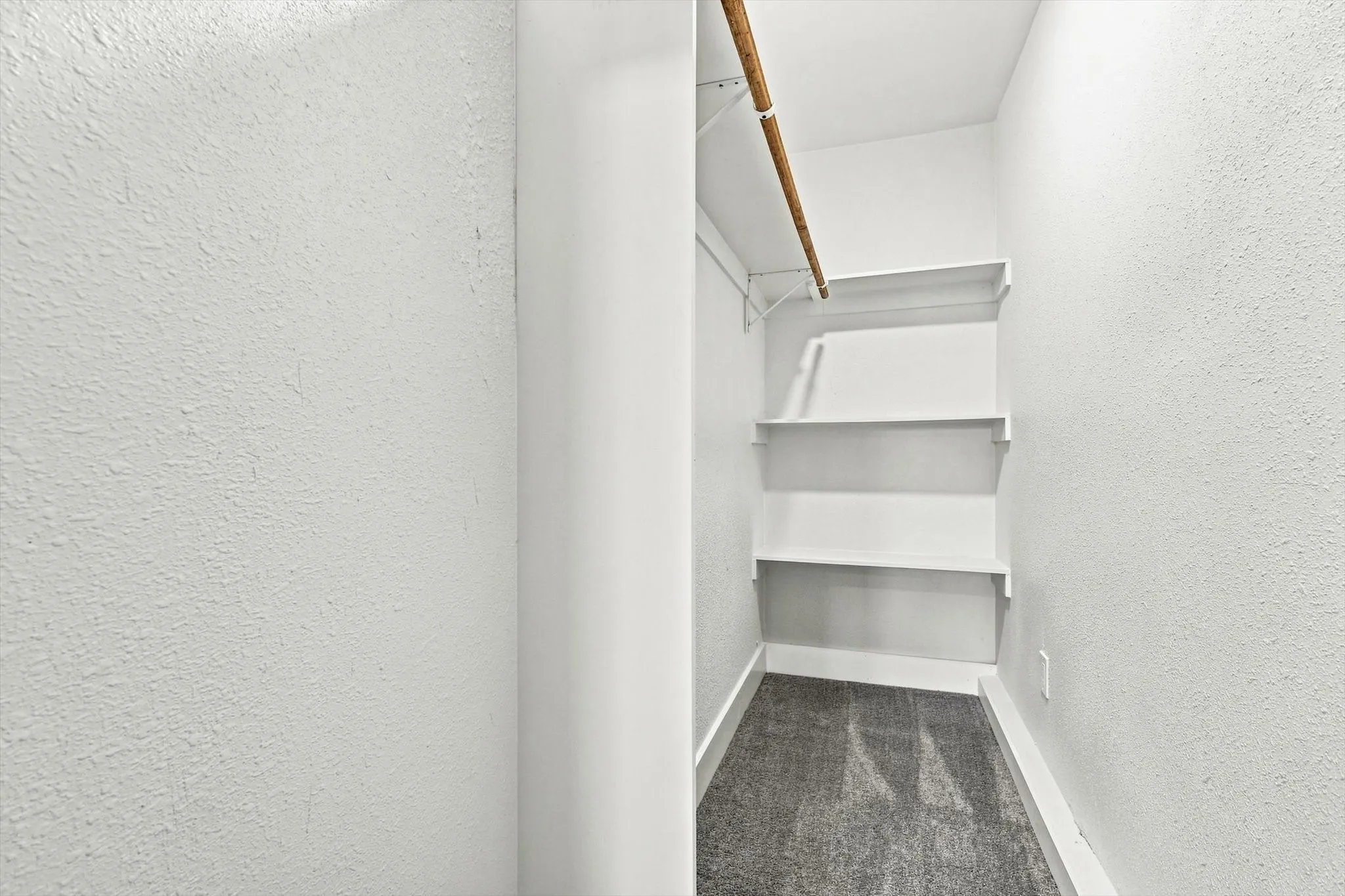 Closet featuring white walls, carpet flooring, a hanging rod, and multiple built-in shelves