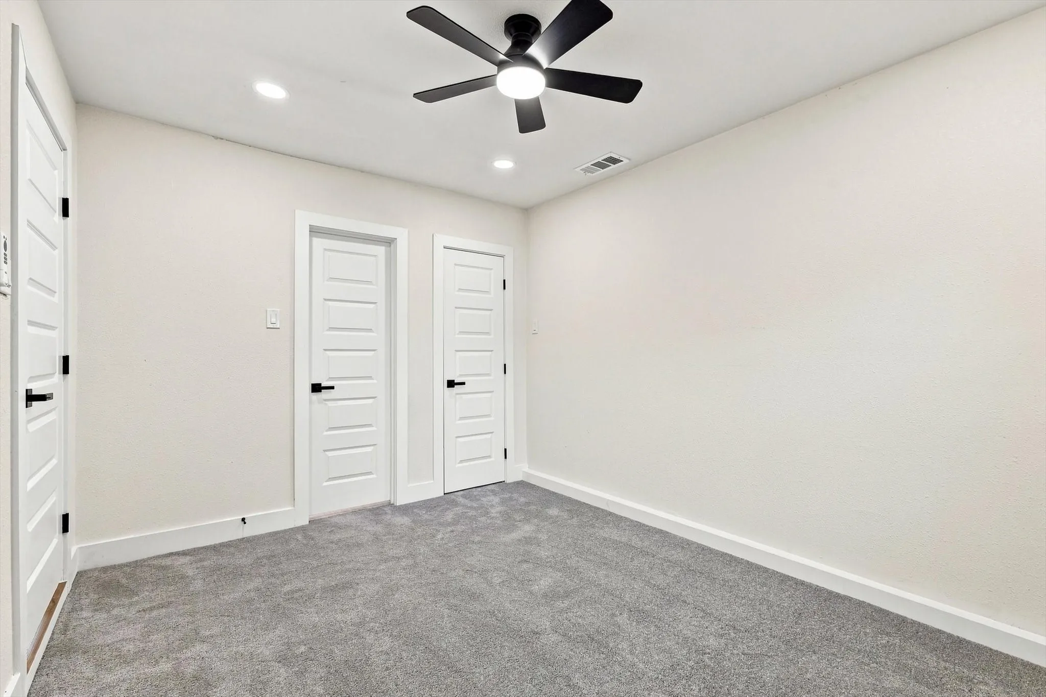 Gray carpeting, white walls, recessed lighting, ceiling fan with light, white paneled doors with black hardware