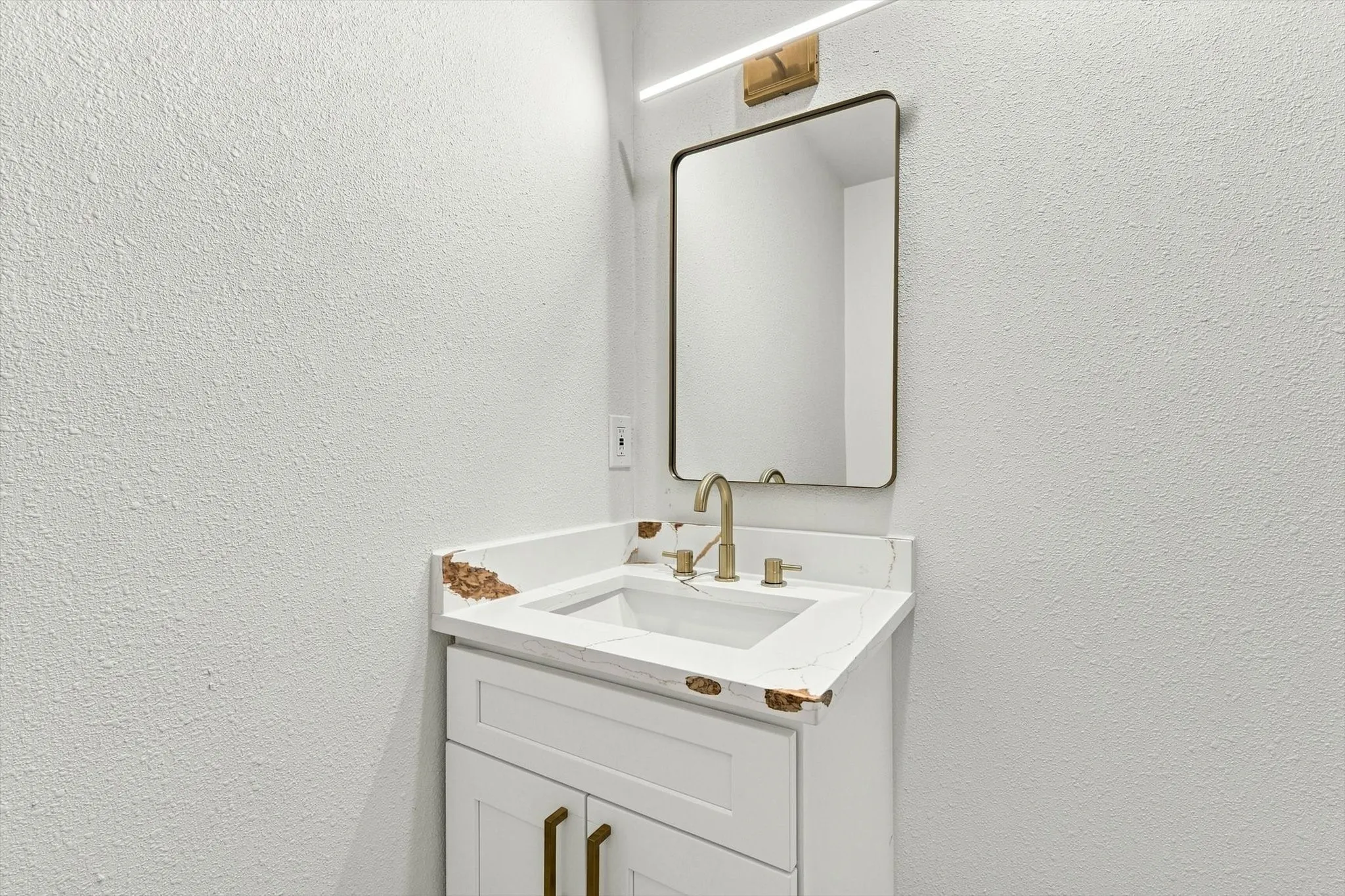 White single vanity with gold-tone hardware, an integrated sink, and a rectangular mirror with a gold-tone frame