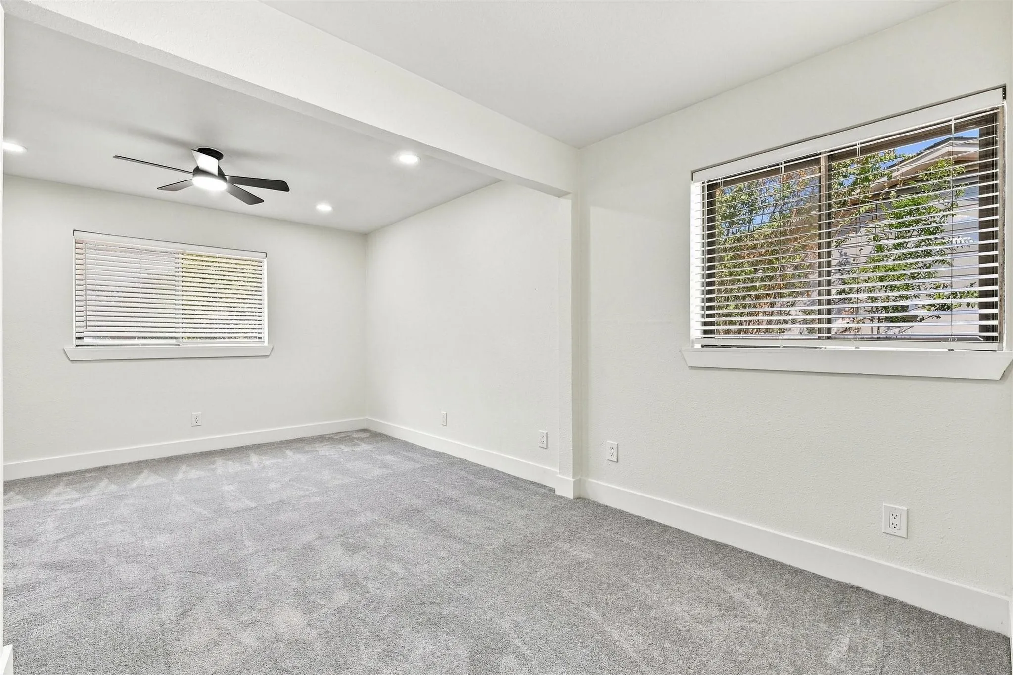 Recessed lighting, ceiling fan, two windows with blinds, and light-toned carpeting