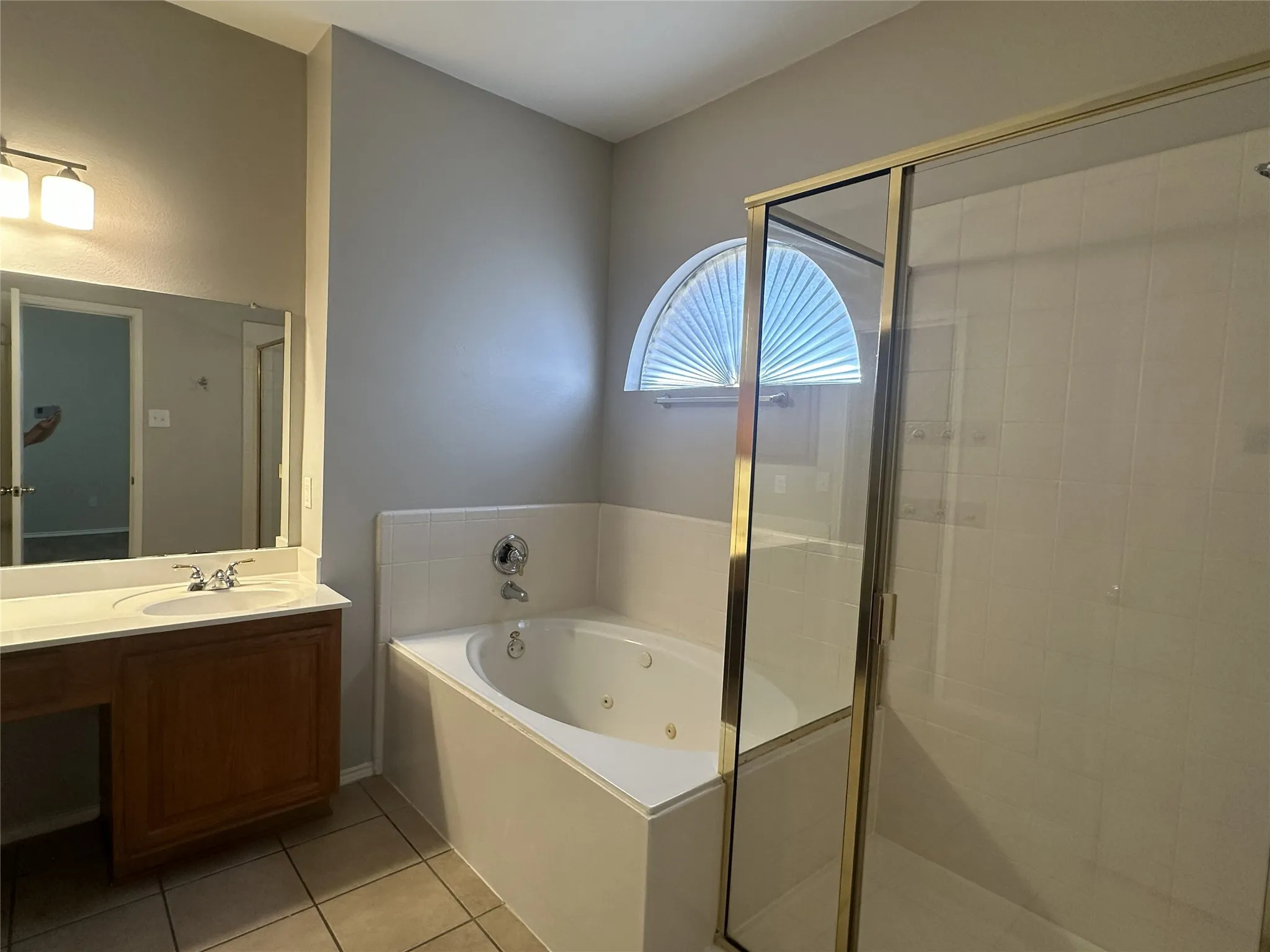 White tiled flooring, vanity with integrated sink, built-in bathtub, and a glass-enclosed shower