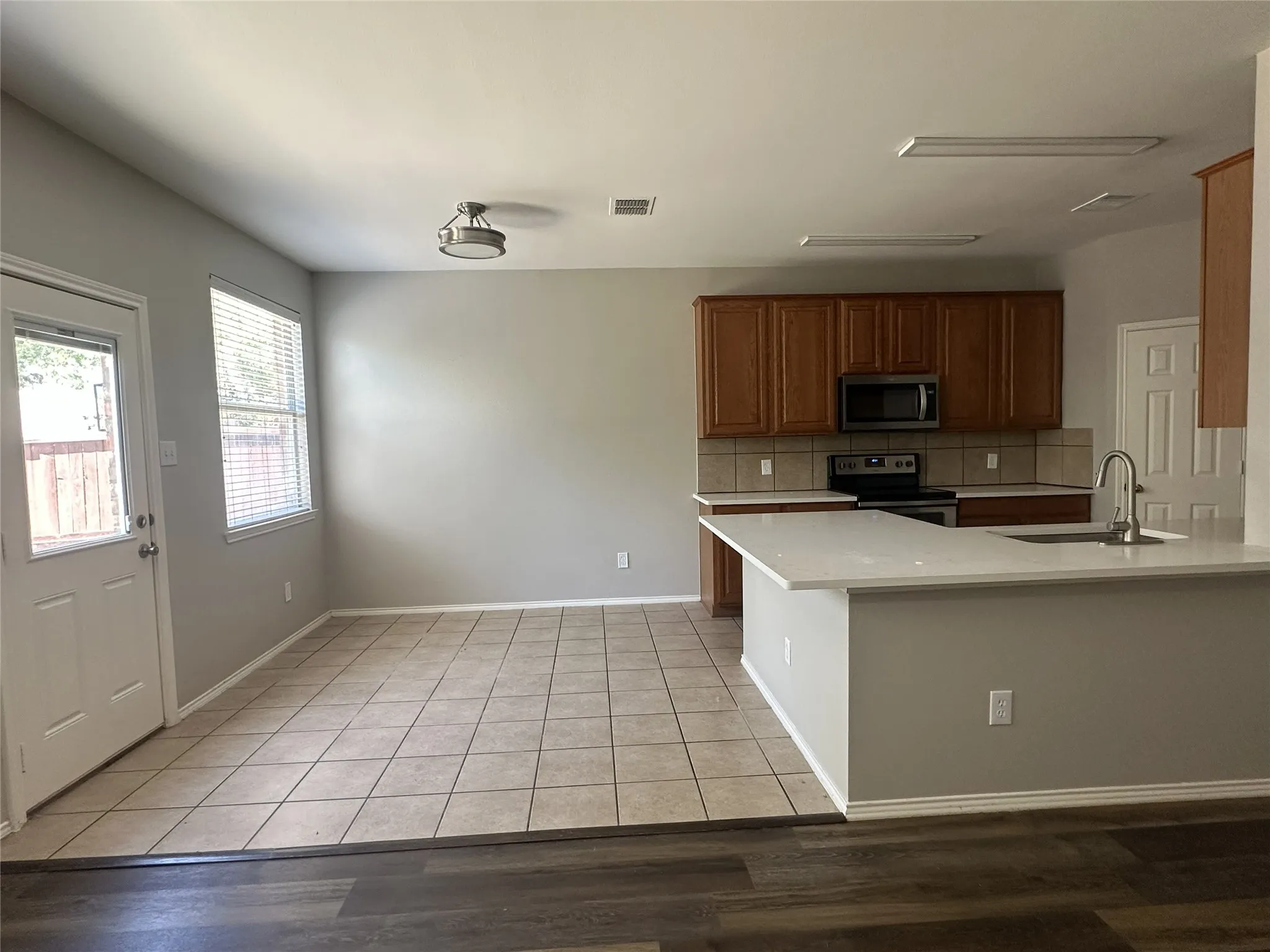 Contemporary kitchen featuring light wood cabinetry, a stainless steel microwave and range, a tile backsplash, and light-toned countertops