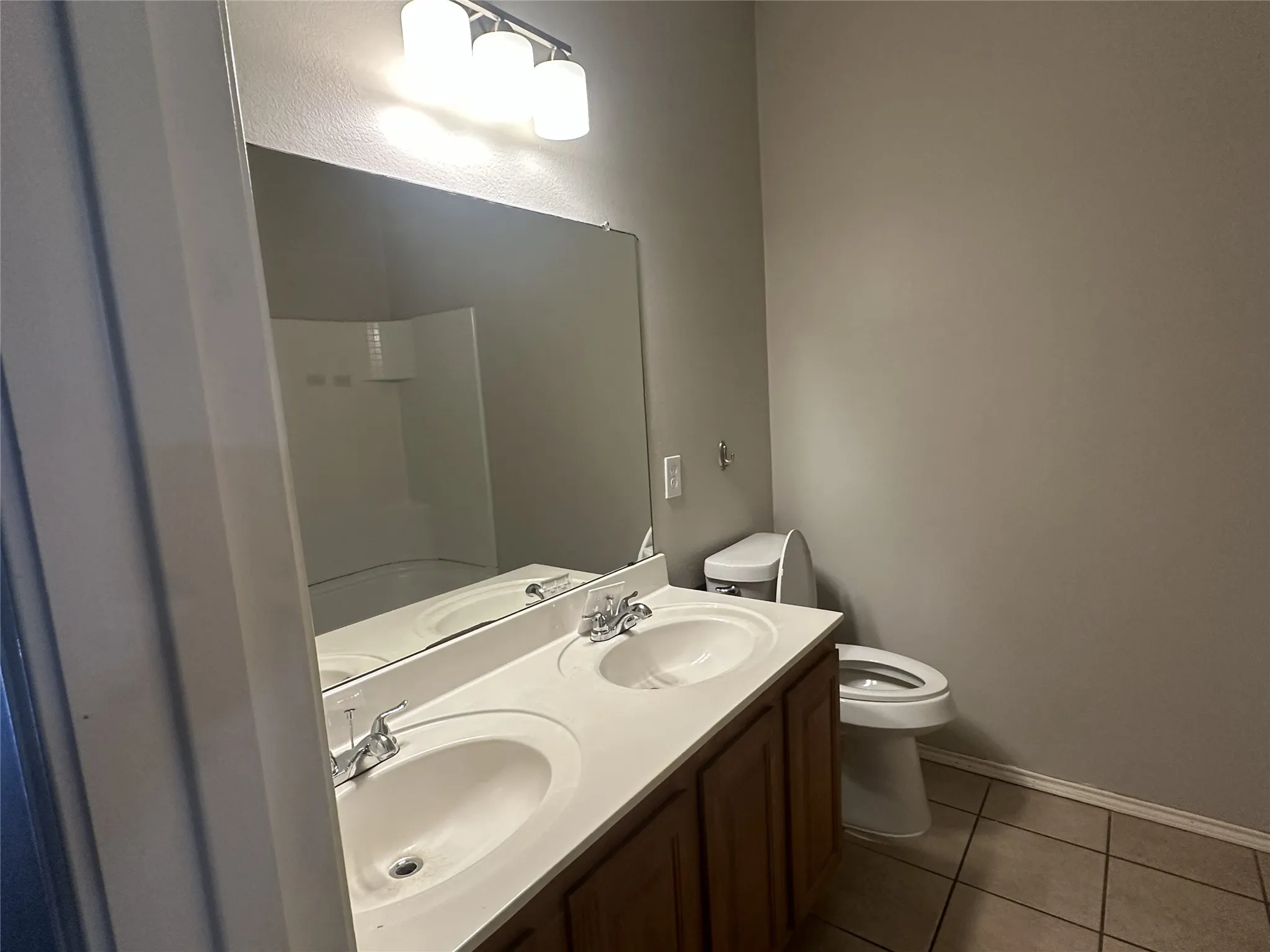 Dual vanity with integrated sinks, wood-finish cabinetry, a large mirror, and three-light fixture