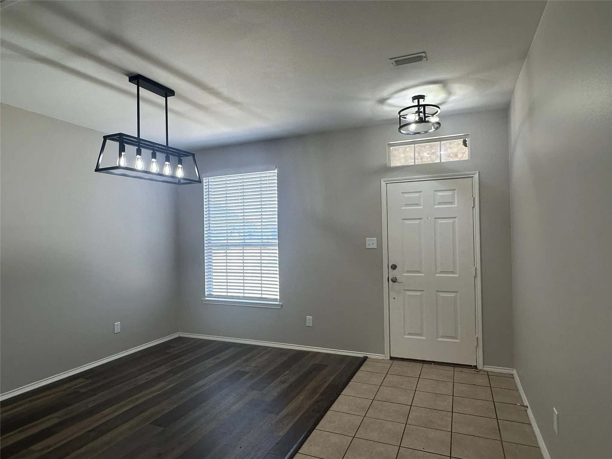 Wood-finish flooring with a contrasting tile entry, contemporary linear chandelier, and a semi-flush mount ceiling light
