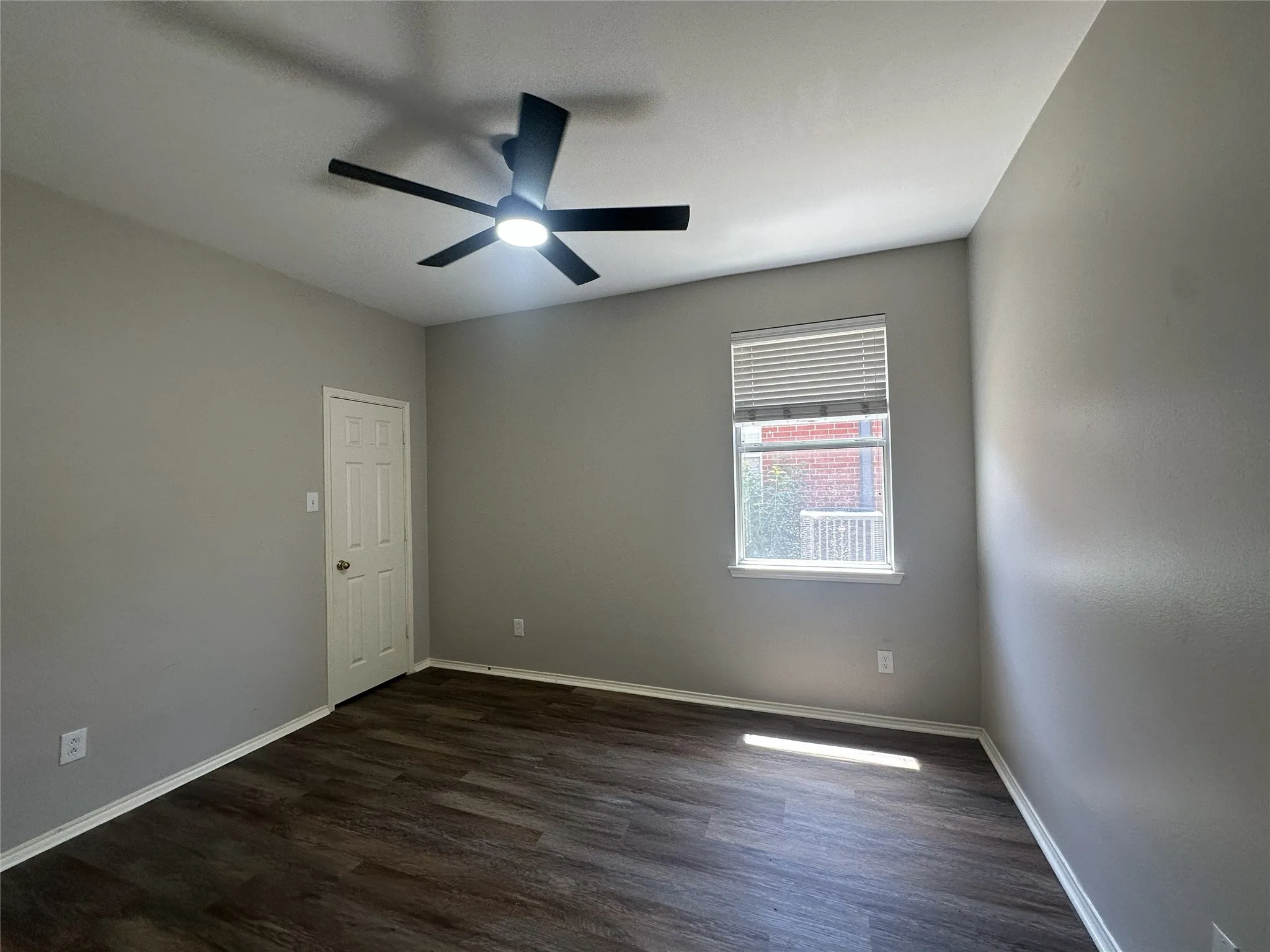 Wood-finish flooring, neutral paint palette, ceiling fan with integrated lighting, window with horizontal blinds, and white trim
