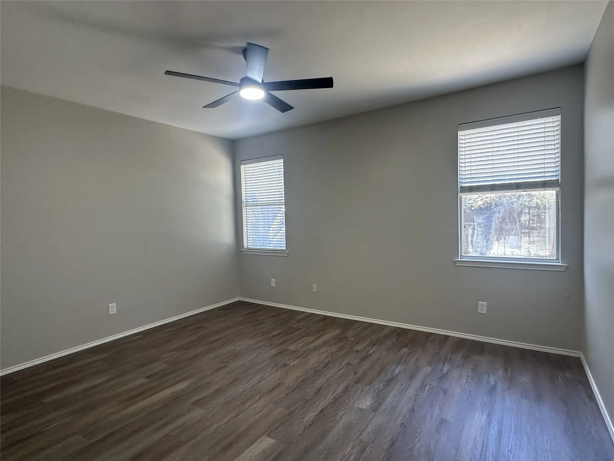Wood-finish flooring, neutral wall paint, ceiling fan with integrated lighting, and dual windows with blinds