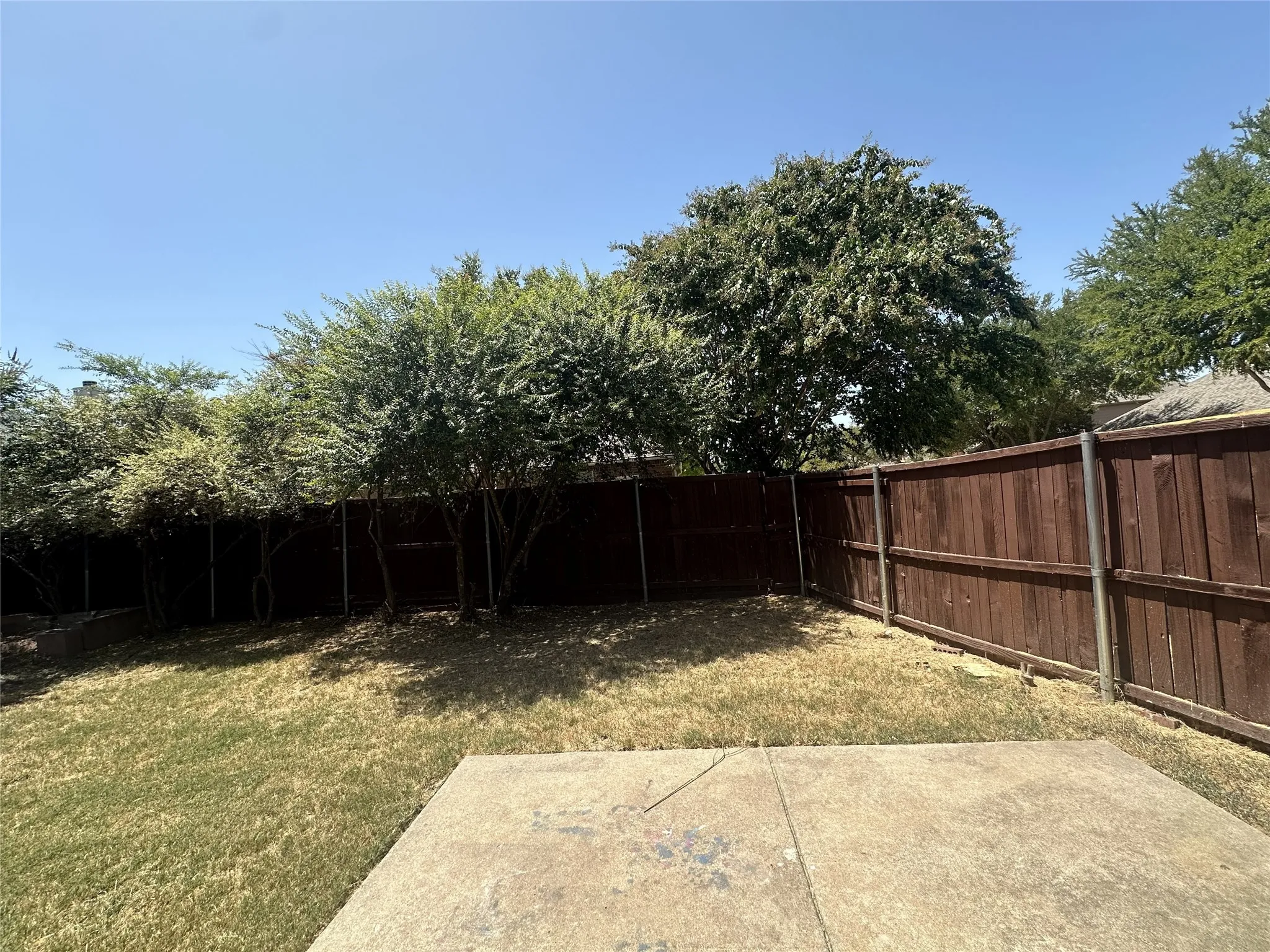 Fenced backyard featuring a concrete patio and mature trees