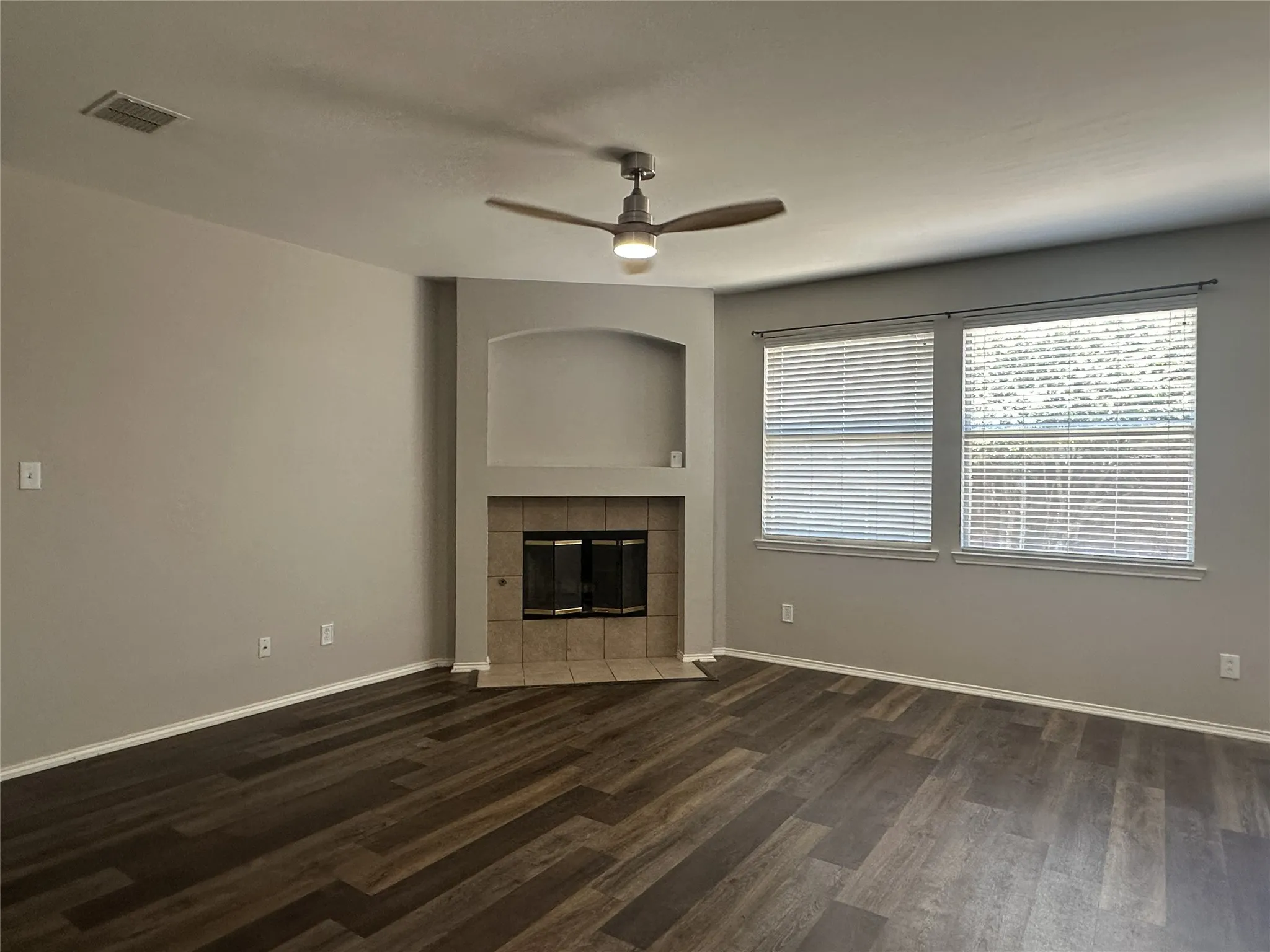 Spacious interior featuring wood-finish flooring, a ceiling fan with integrated lighting, and a fireplace with a tile surround and hearth