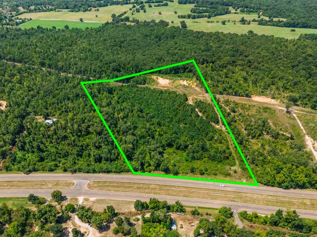 Expansive land parcel featuring dense tree coverage, a cleared area, and direct road frontage
