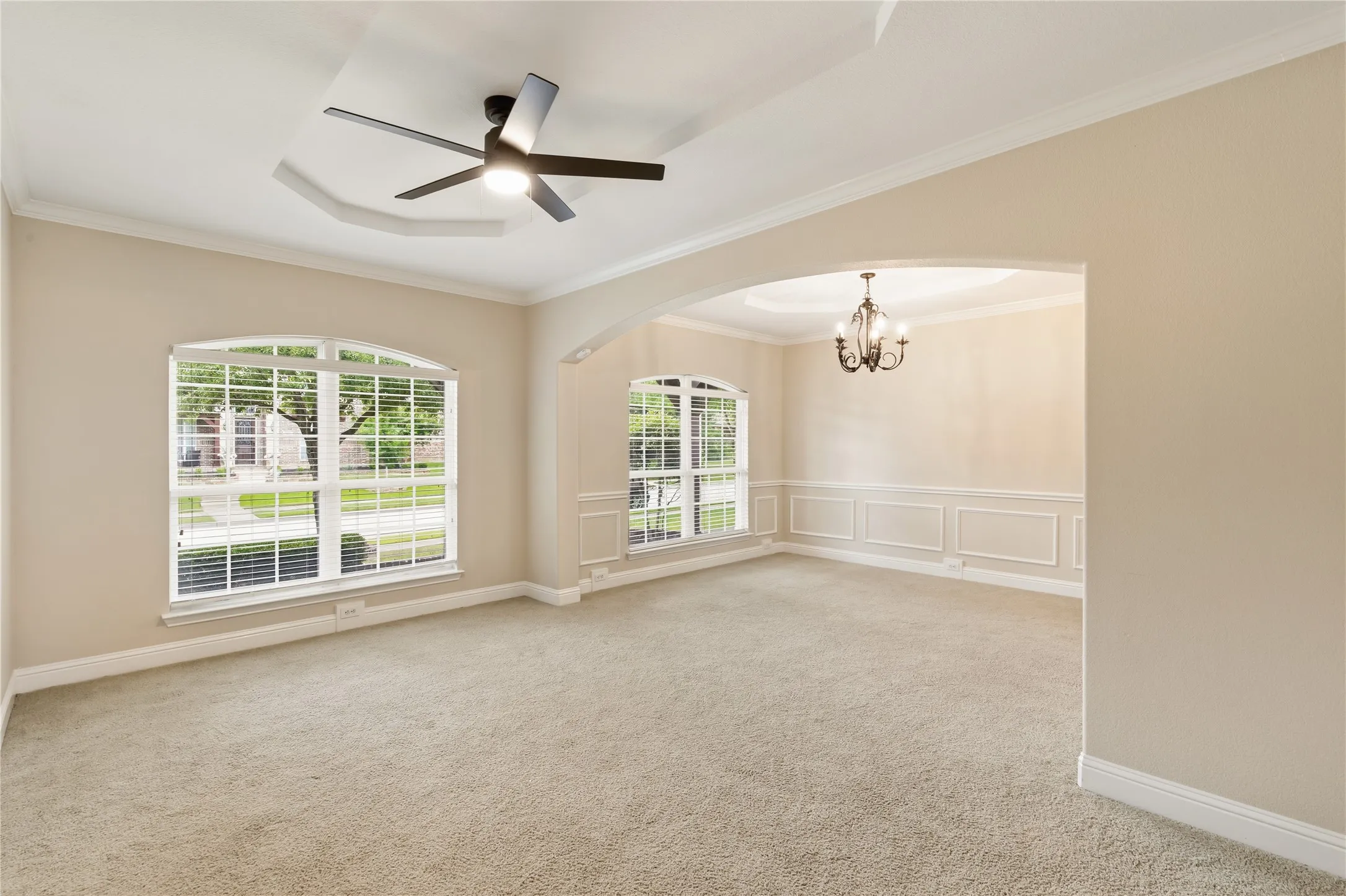 Spacious interior room featuring a tray ceiling with a modern ceiling fan, arched windows, and soft carpet flooring
