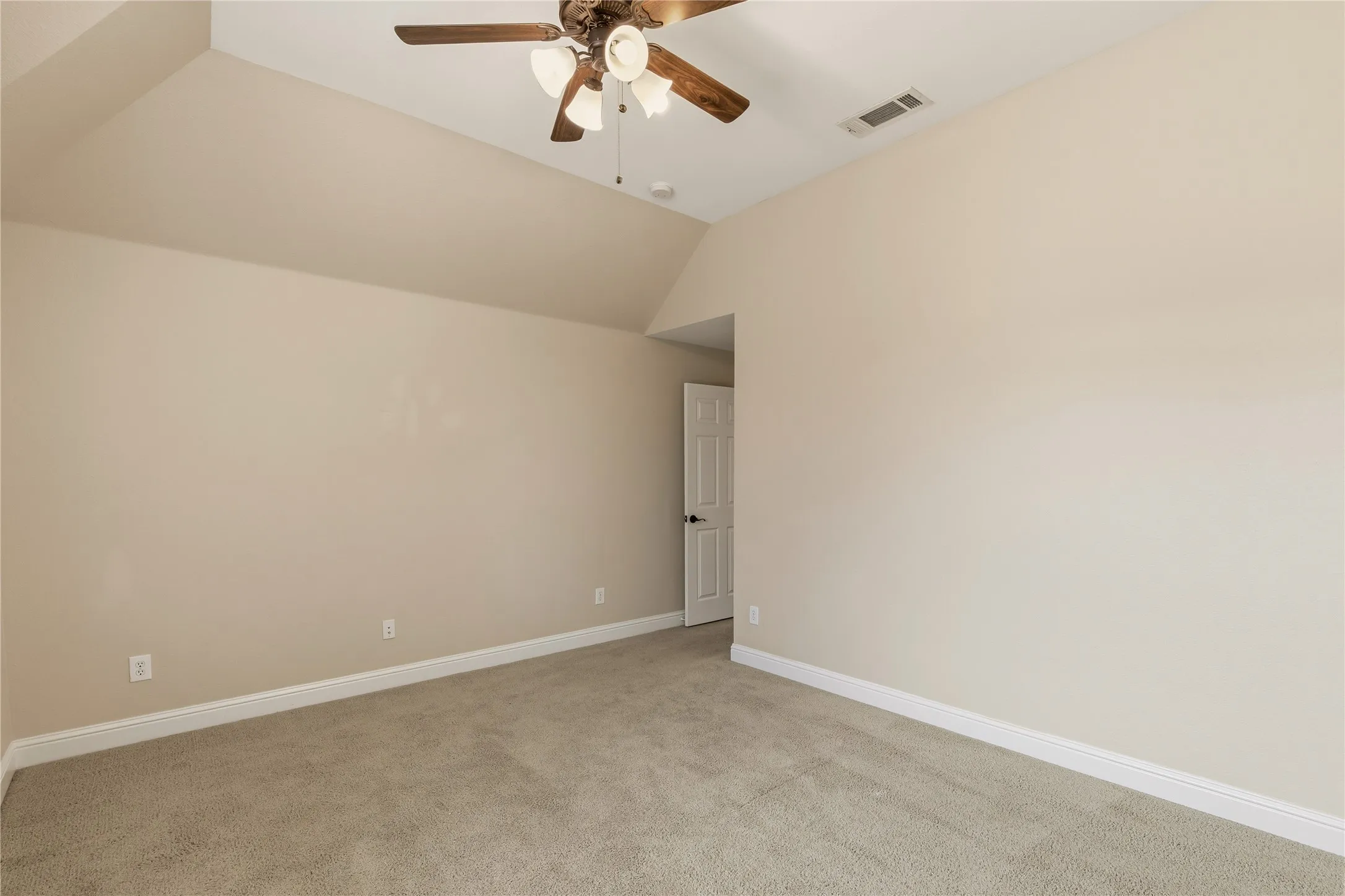 Carpeted interior room featuring neutral wall tones, white baseboards, and a vaulted ceiling