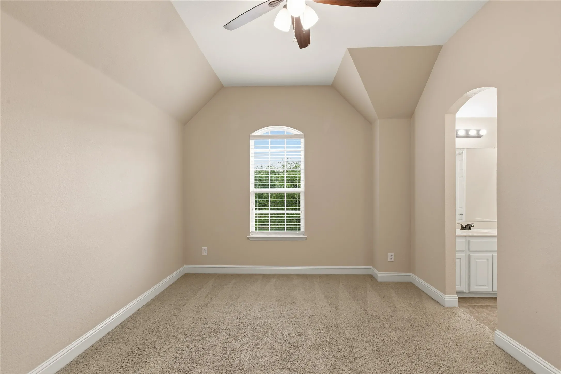 Carpeted room featuring a vaulted ceiling and arched window